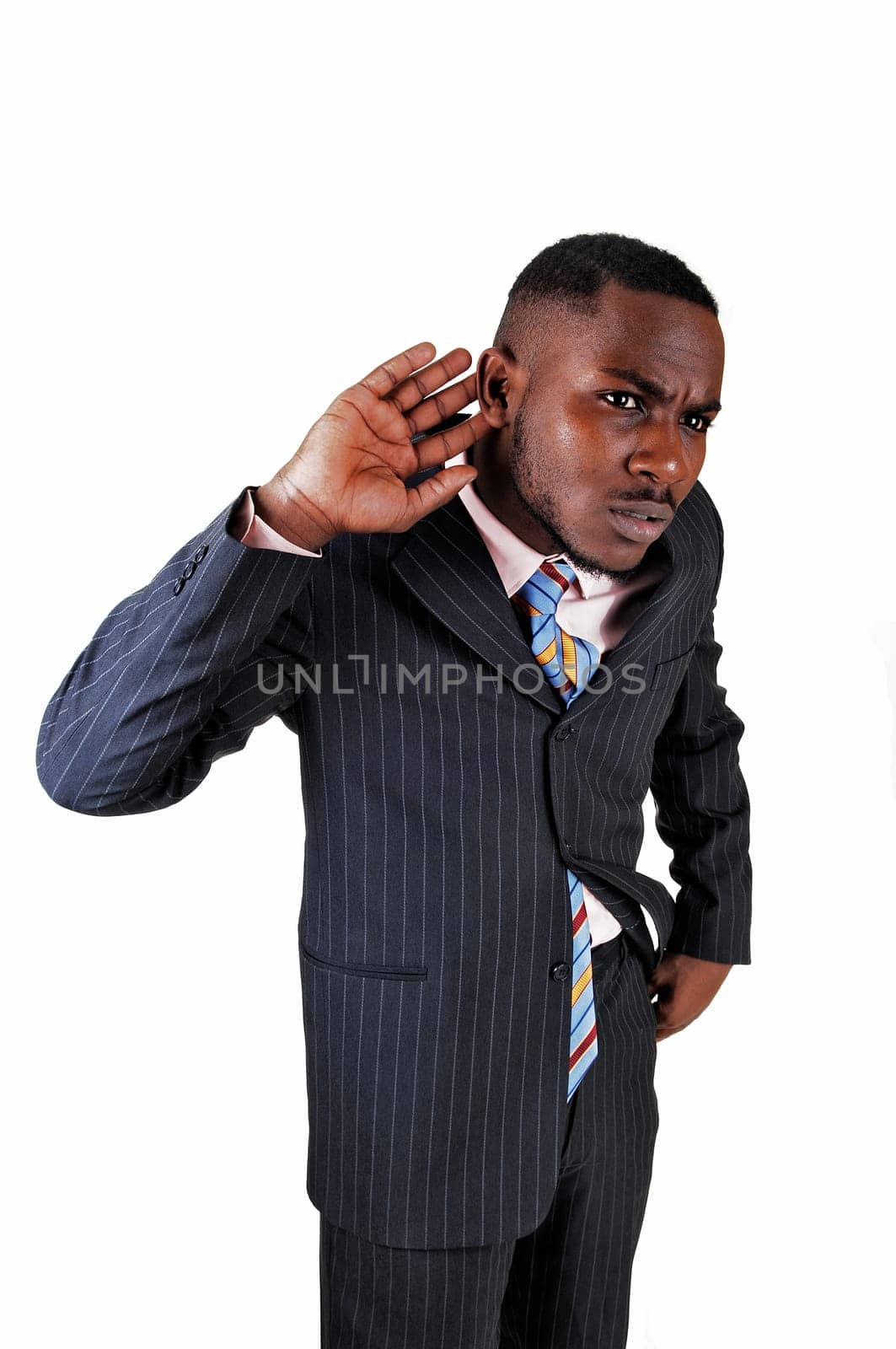 A young black business man in a blue suit and tie holding his hand on.his ear to listens closely, for white background..