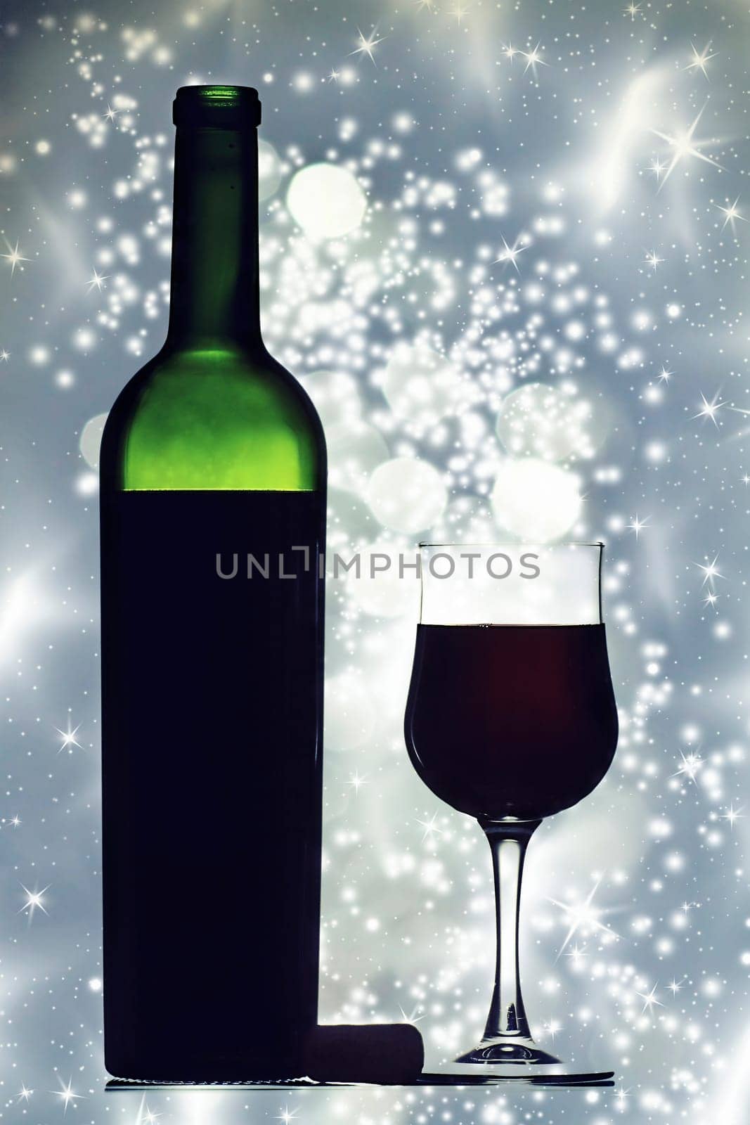 Glass and bottle of red wine against holiday lights