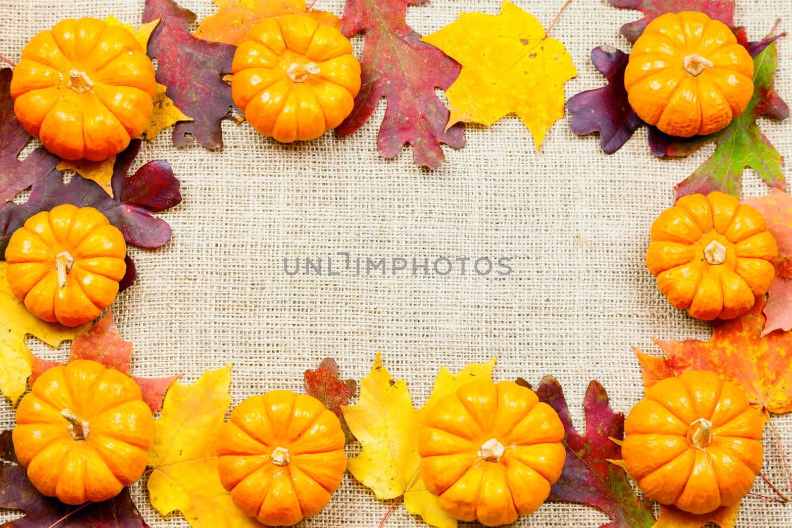 Fall-themed background of burlap, dry leaves and pumpkins