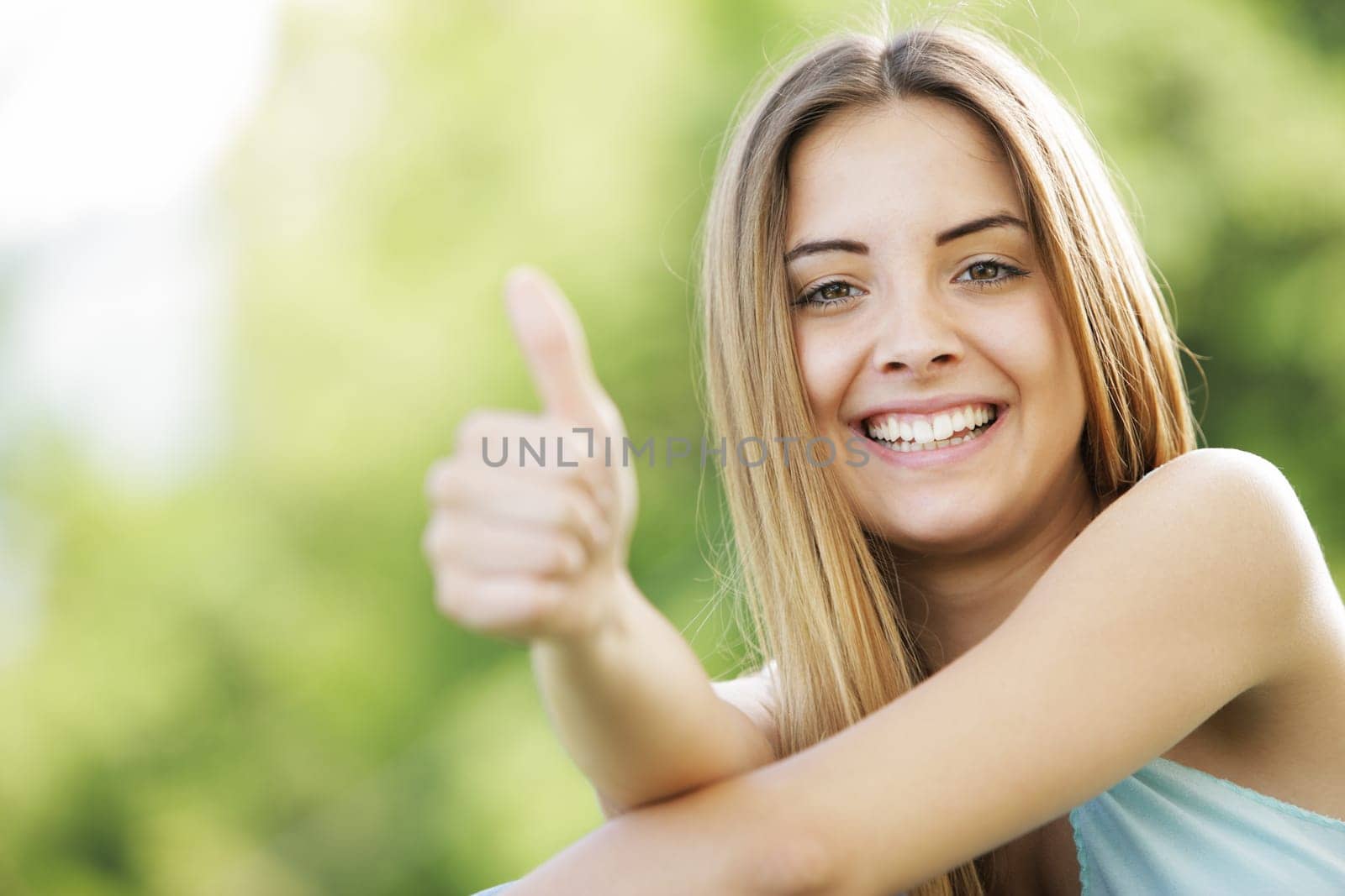 Young smiling blond female outdoors showing thumb up sign