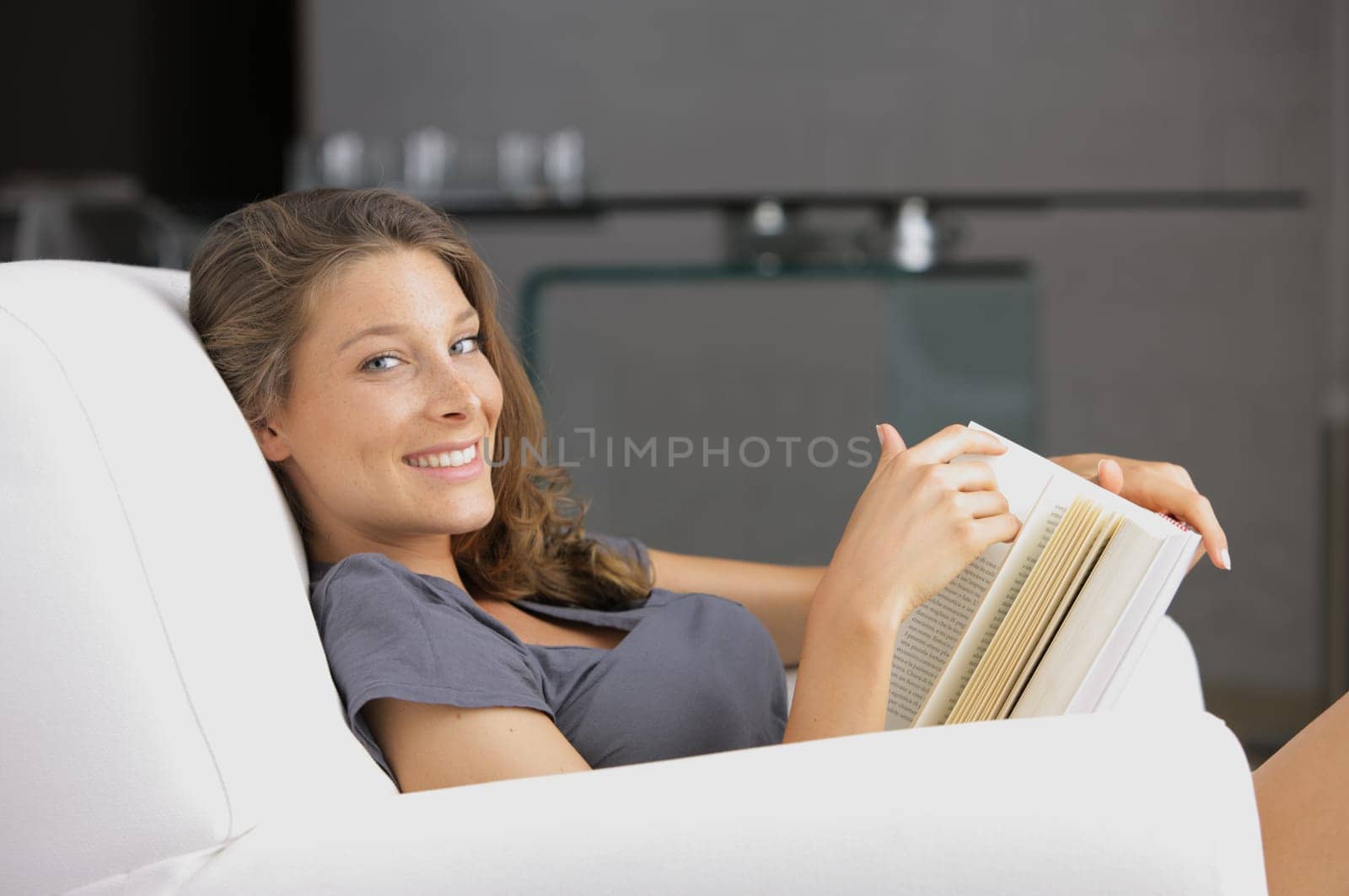 Young smiling woman reading a book in a white armchair