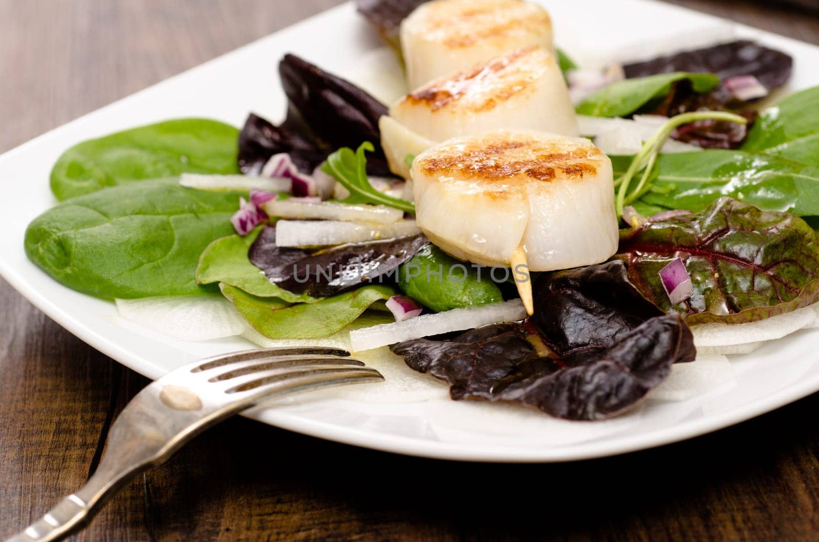 Scallops fried on a wooden skewer with salad