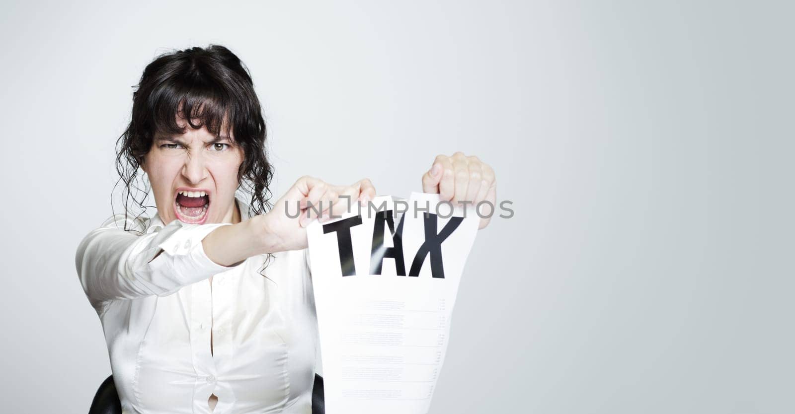 Young desperate woman at her paperwork-covered desk ripping up a tax form staring at the camera