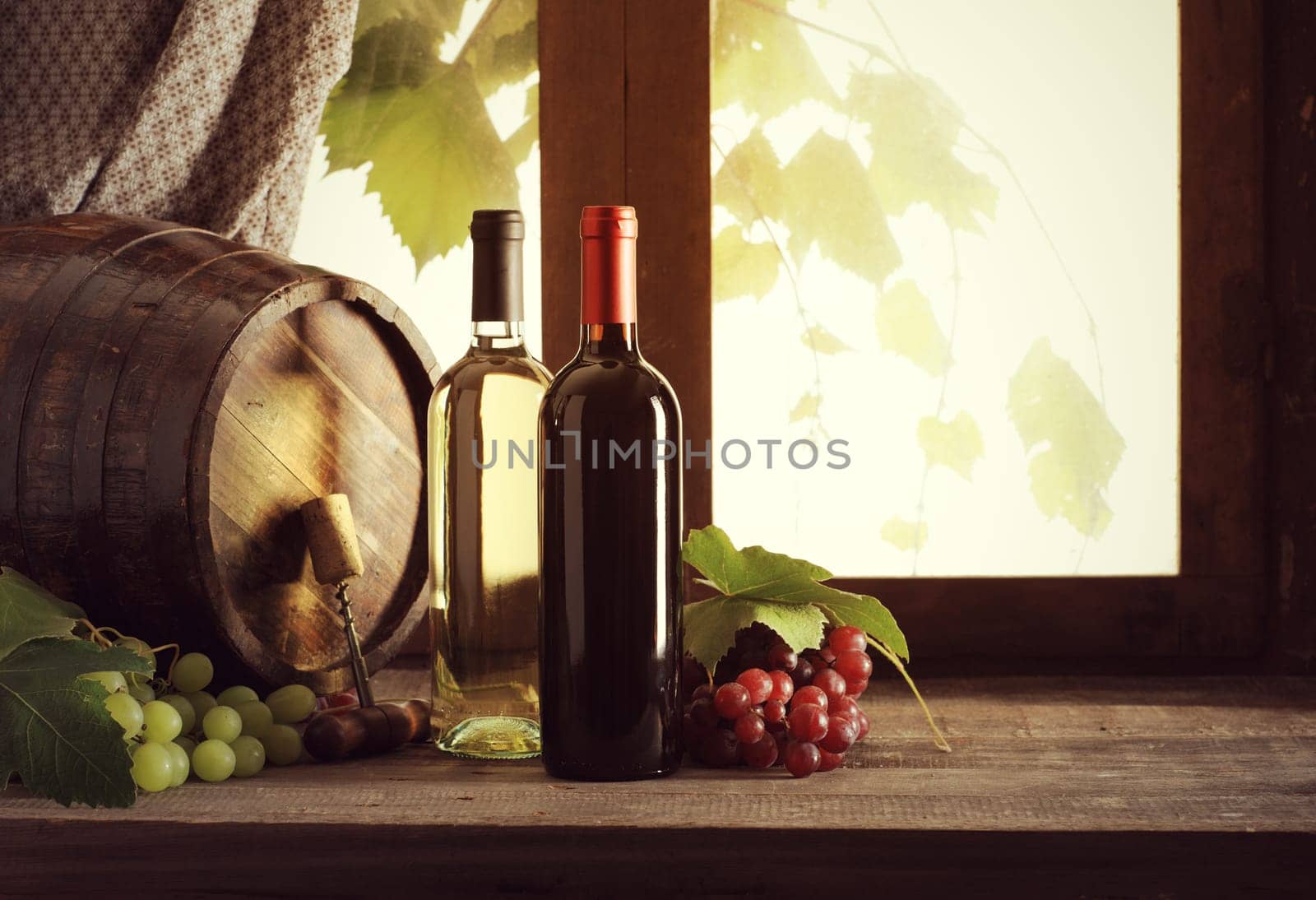 Wine bottles with grapes and barrel on old wooden table