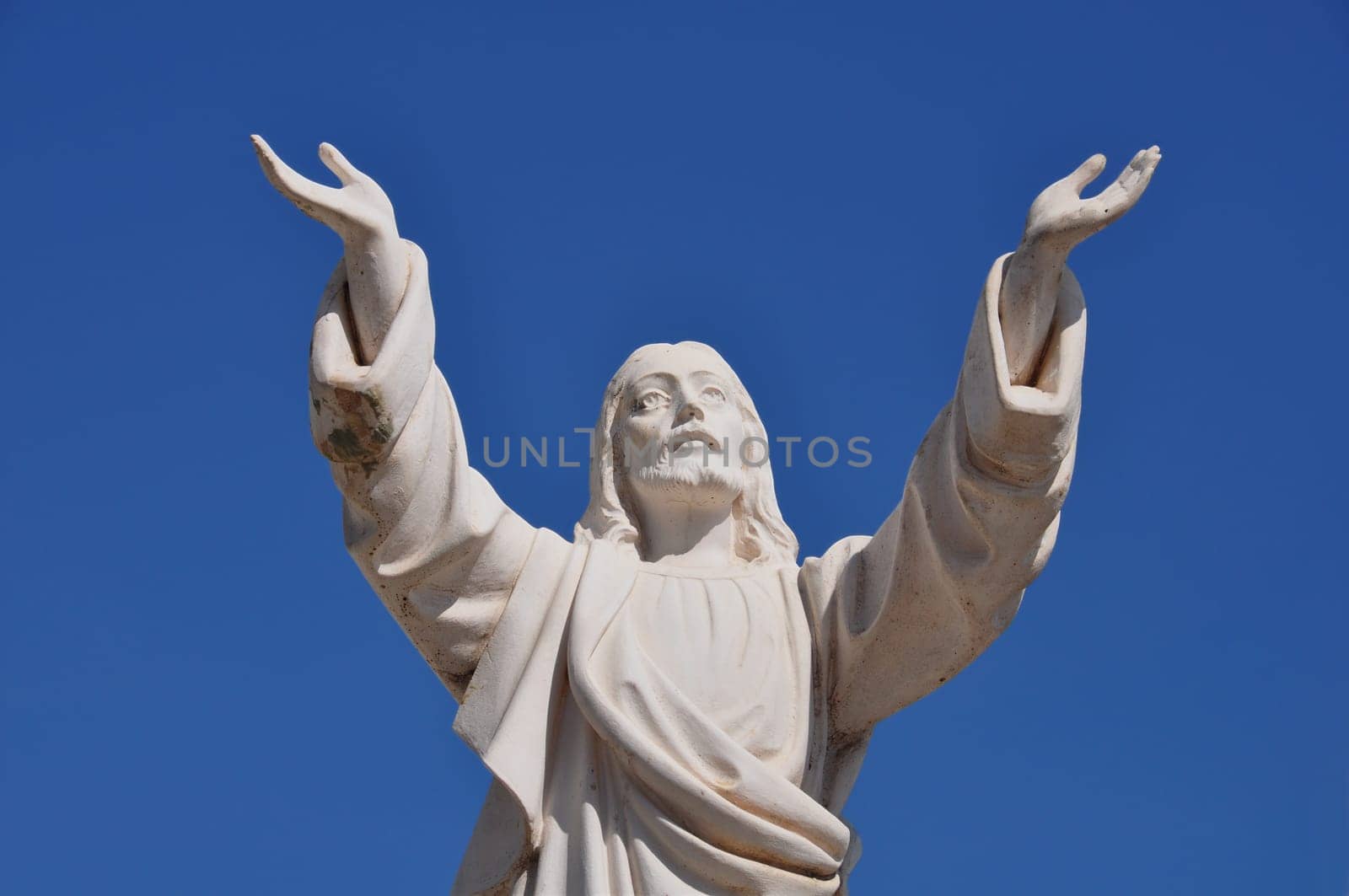 Jesus Christ with hands raised in blessing under blue sky. Marble funerary statue.