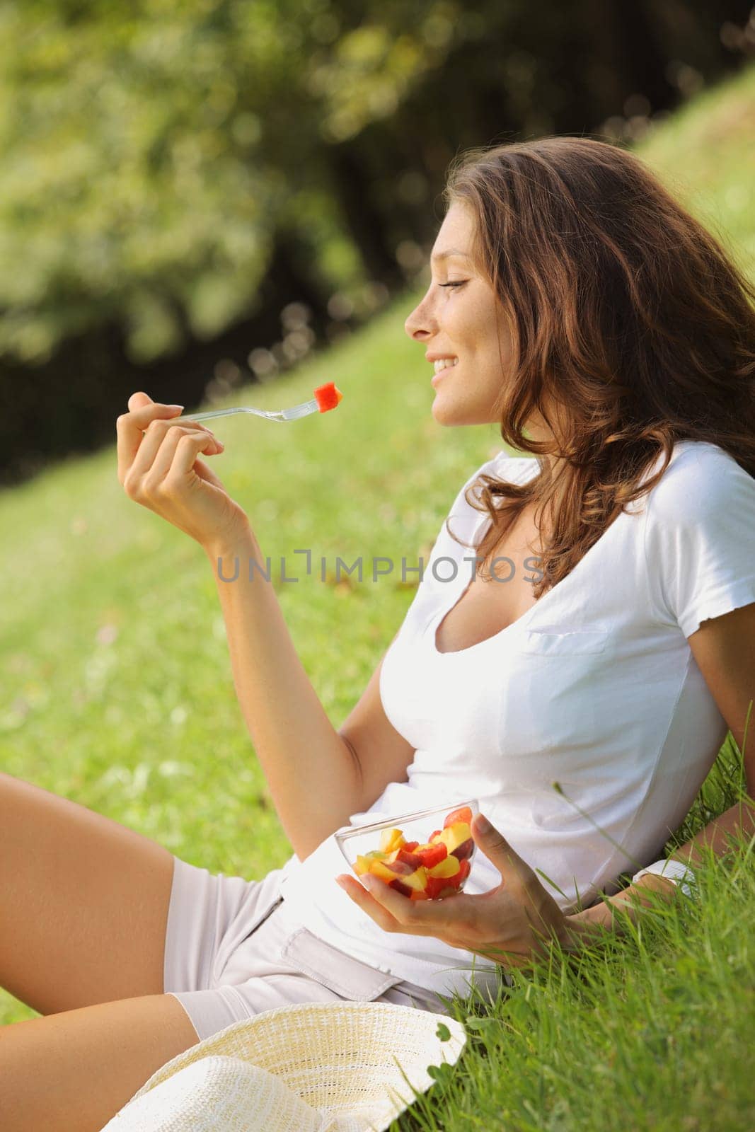 Beautiful woman eating fruit salad on a lawn