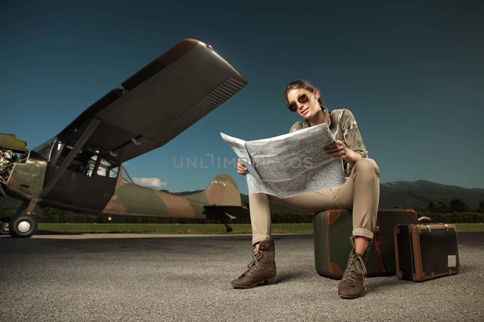 Beautiful young woman sitting on a suitcase, looks at a map. Airplane in the background