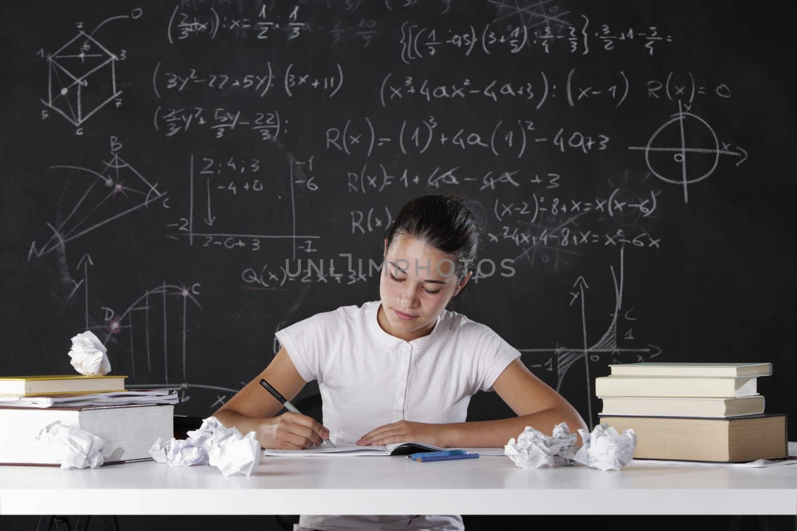 Young student writes in the notebook, in the background a blackboard full of math formulas