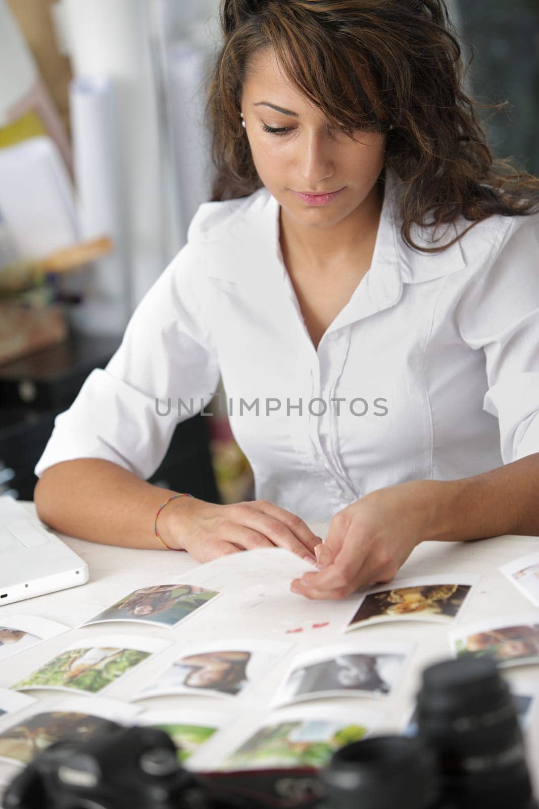 Female photographer examines the photographs, is sitting at her desk in the office