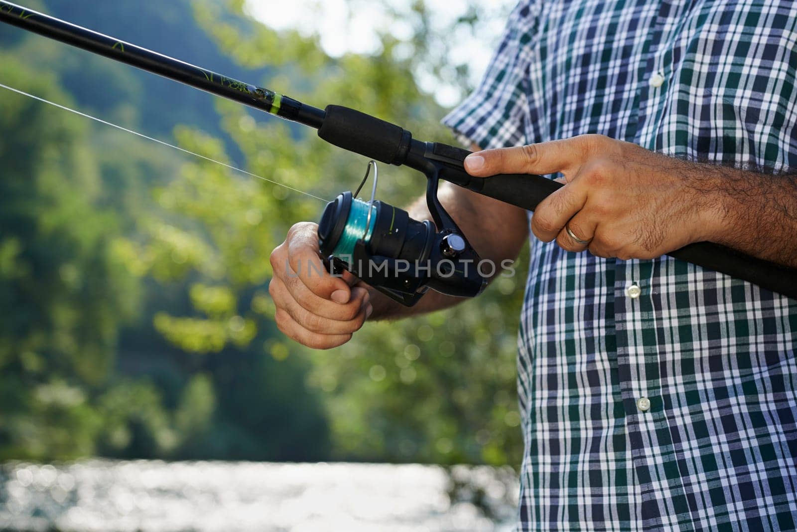 closeup of fisher on river with hands on reel, relaxing and fishing trout