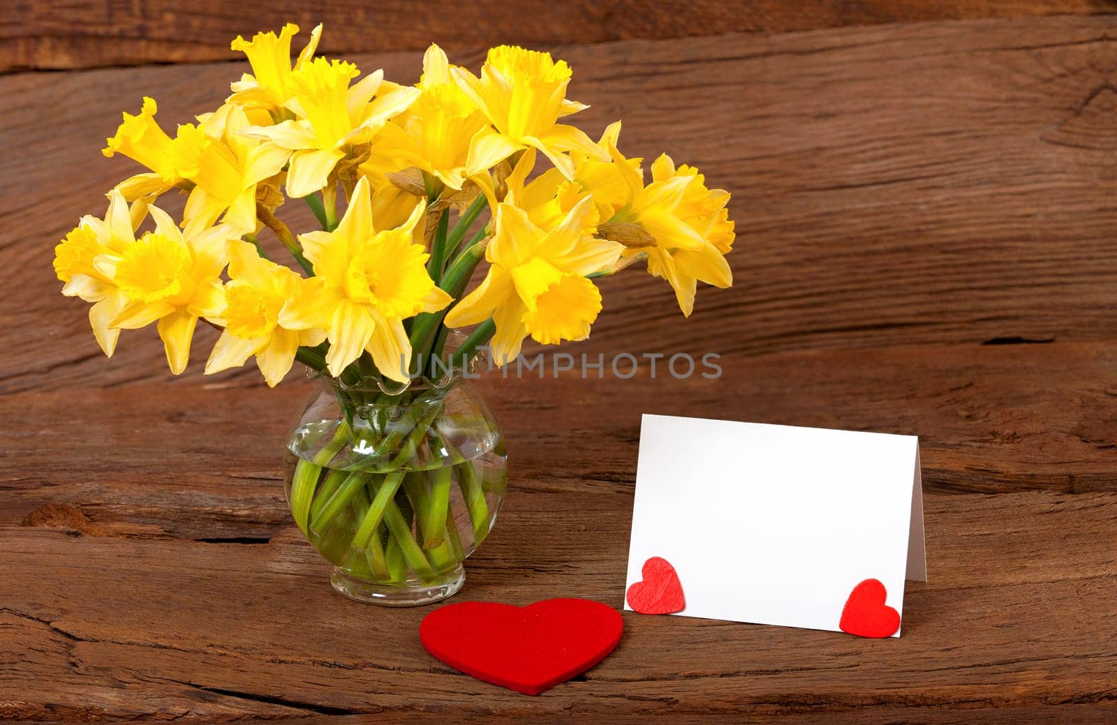 Blank white card with text space next to a bouquet of flowers on a rustic wooden surface