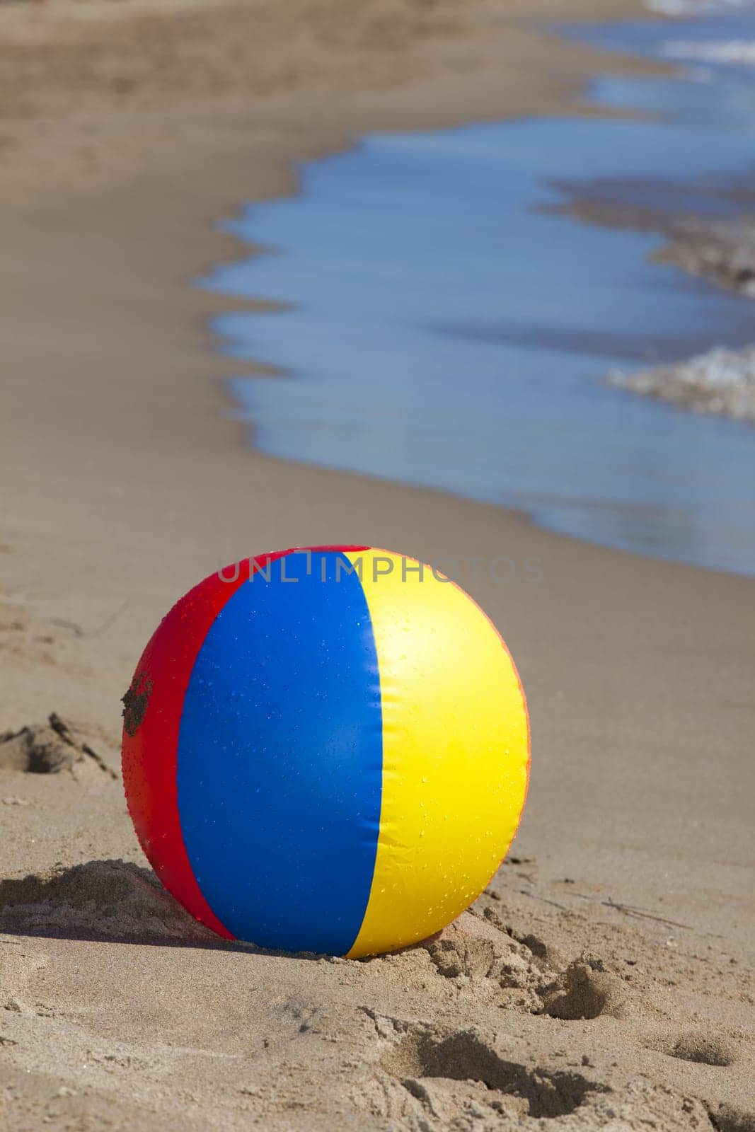 Water polo with water drops lies on the beach in the background the sea with waves can be seen