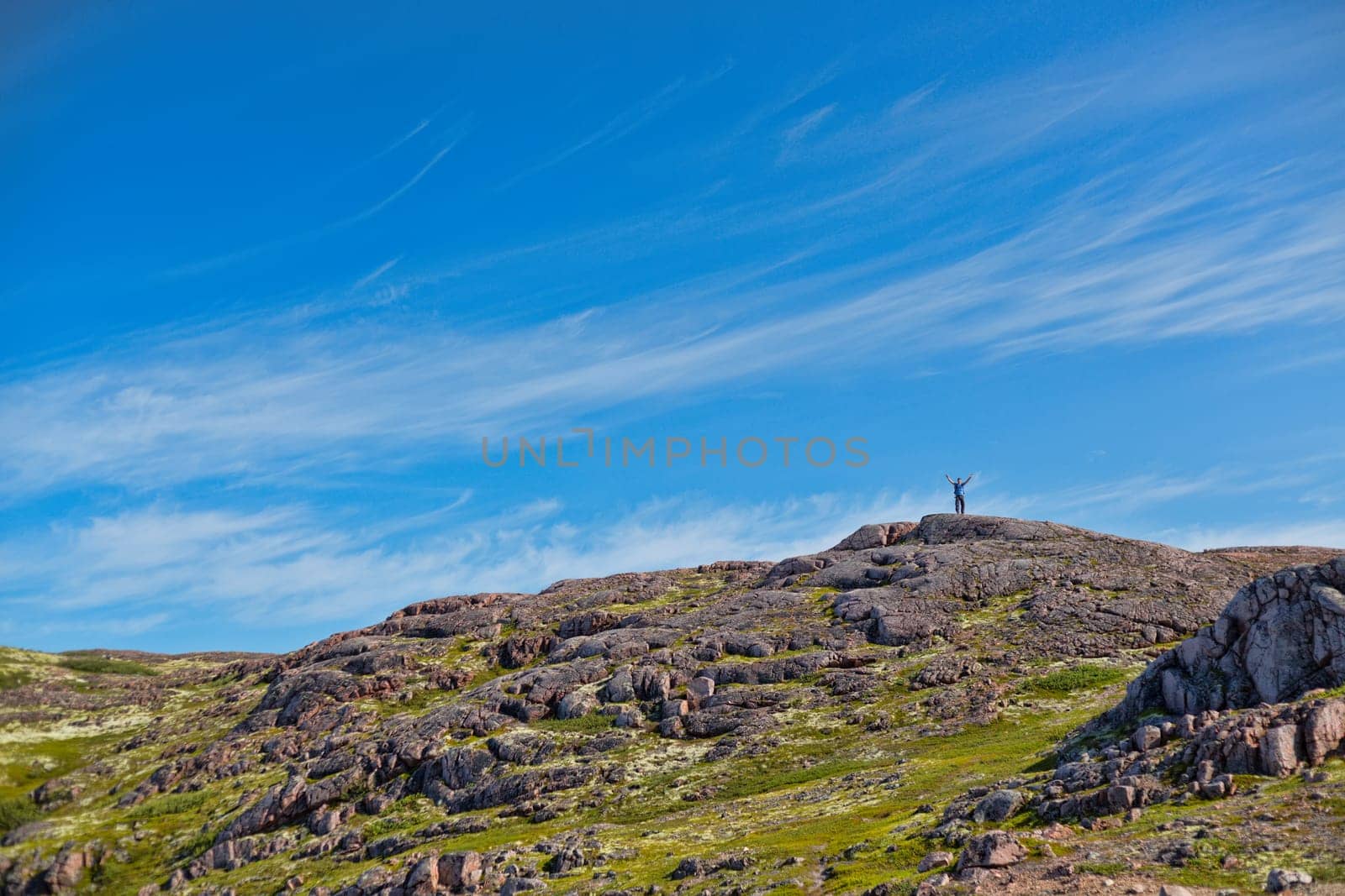 Man with a backpack on a mountain spread wide his hands in the summer against a blue sky with clouds