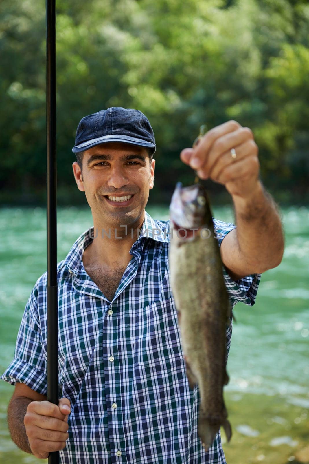 mid adult fisherman on holidays on river, relaxing and fishing trout. Focus on background