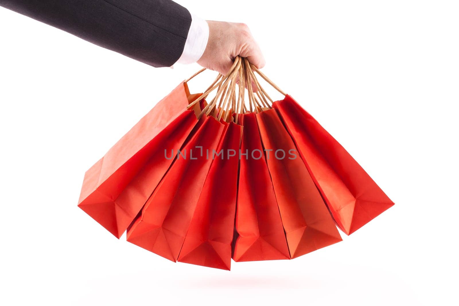 Man's arm in a suit and white shirt holding six red shopping bags on a white background
