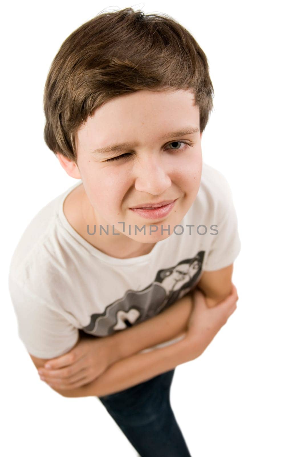 Upper body portrait of a young male teenager in a T-shirt and crossed arms in front of a white background squinting at the camera from elevated view