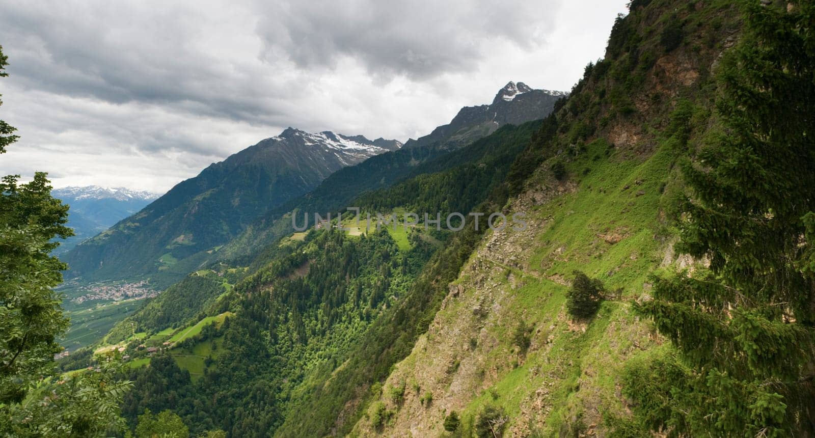 Panoramic view from the Hochmuth / South Tyrol cable car mountain station in the Merano Valley with steep slope and narrow footpath under cloudy skies in summer 2013