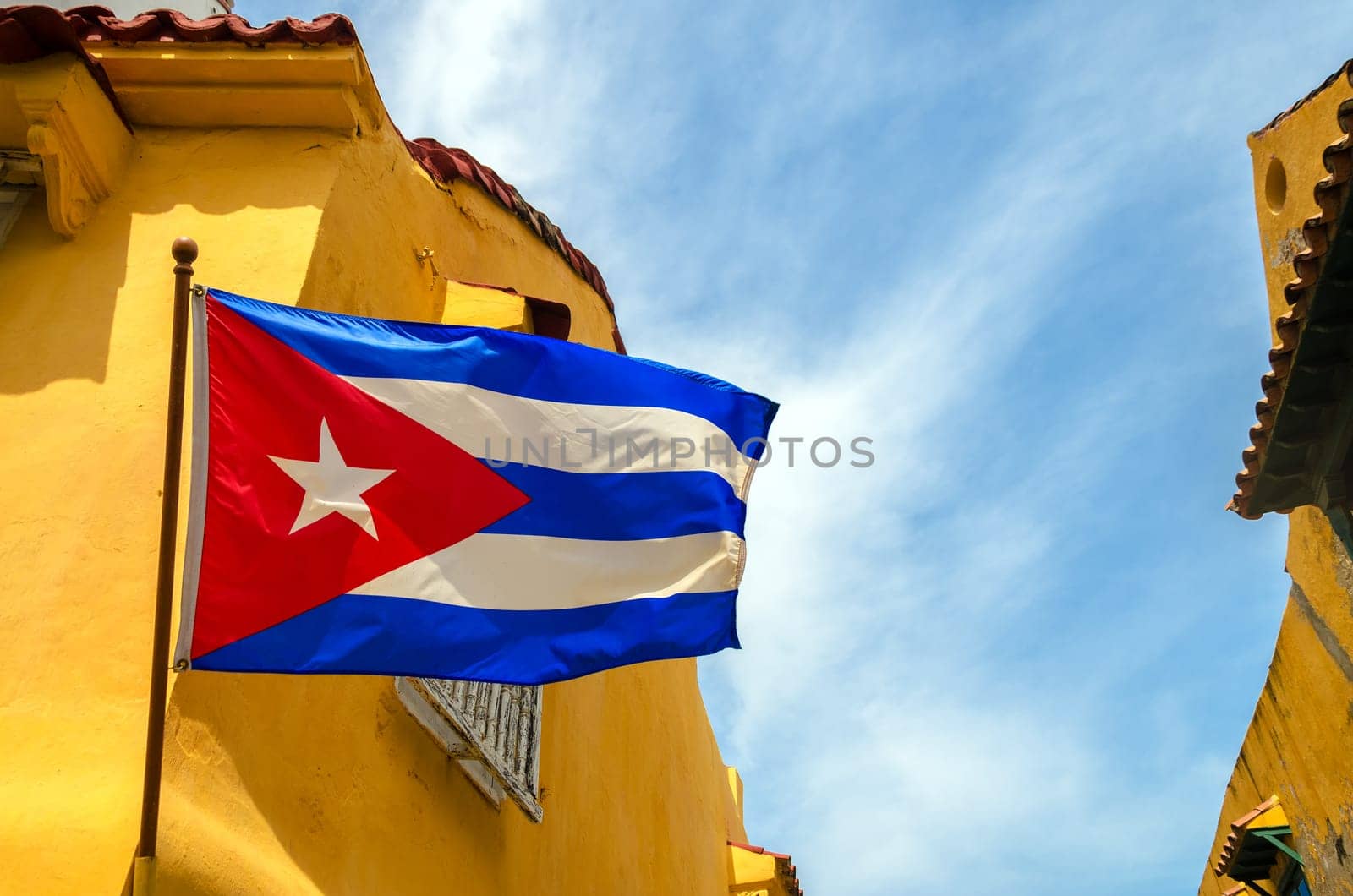 Cuban flag set against blue sky and yellow colonial buildings