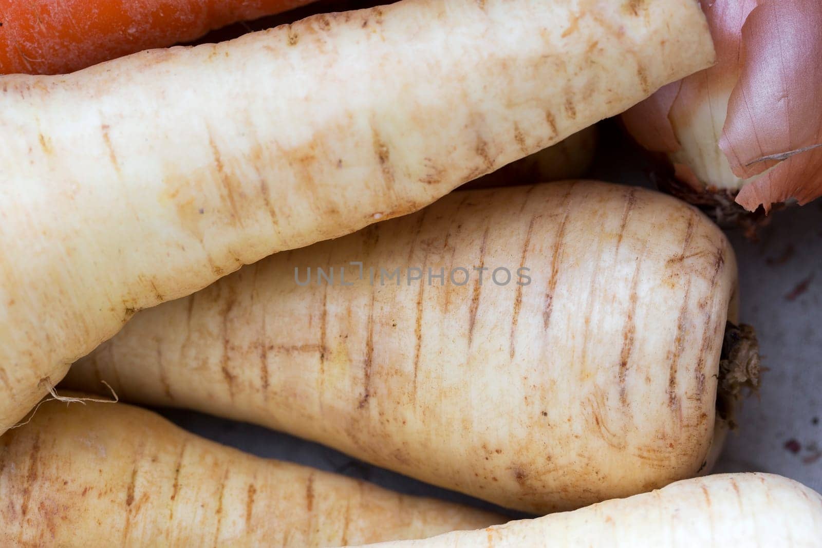 Close up of raw parsnips, with other vegetables barely visible.