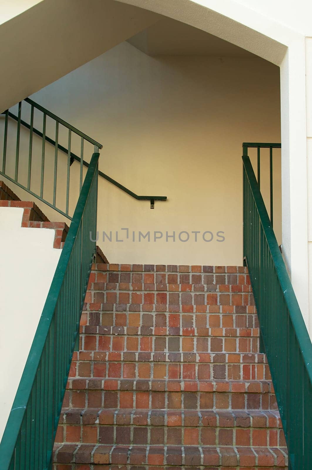 Looking up at a brick stair way with green railings.