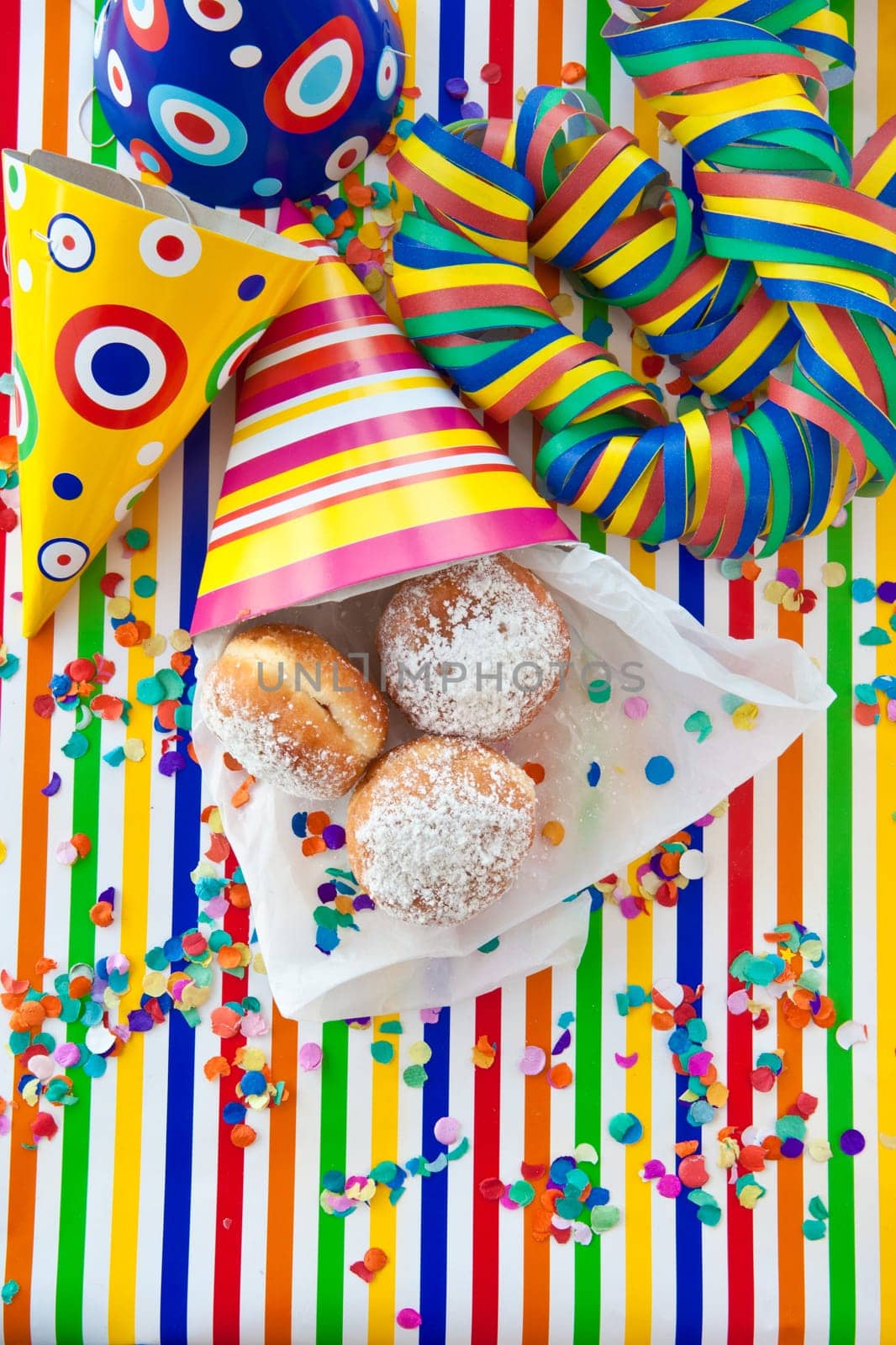 Fresh fritters in colorful bag on striped background