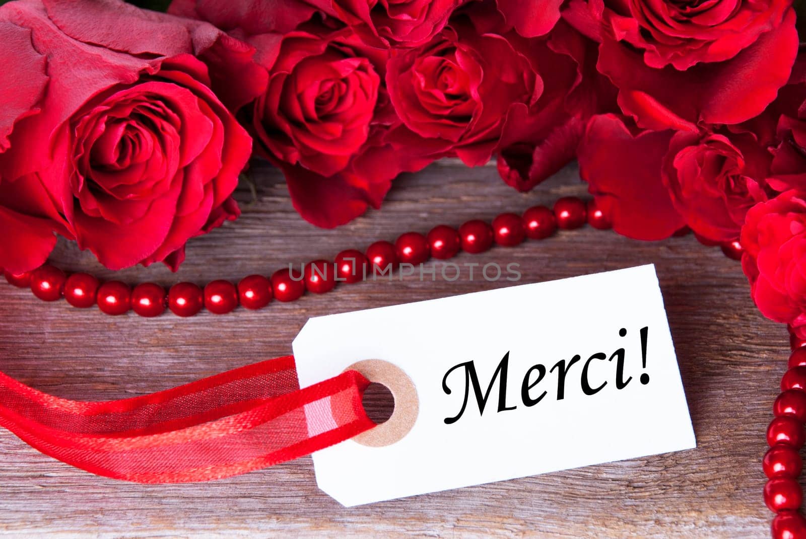 A Background with Red Roses and a White Ticket with the French Word Merci on it Which Means Thanks
