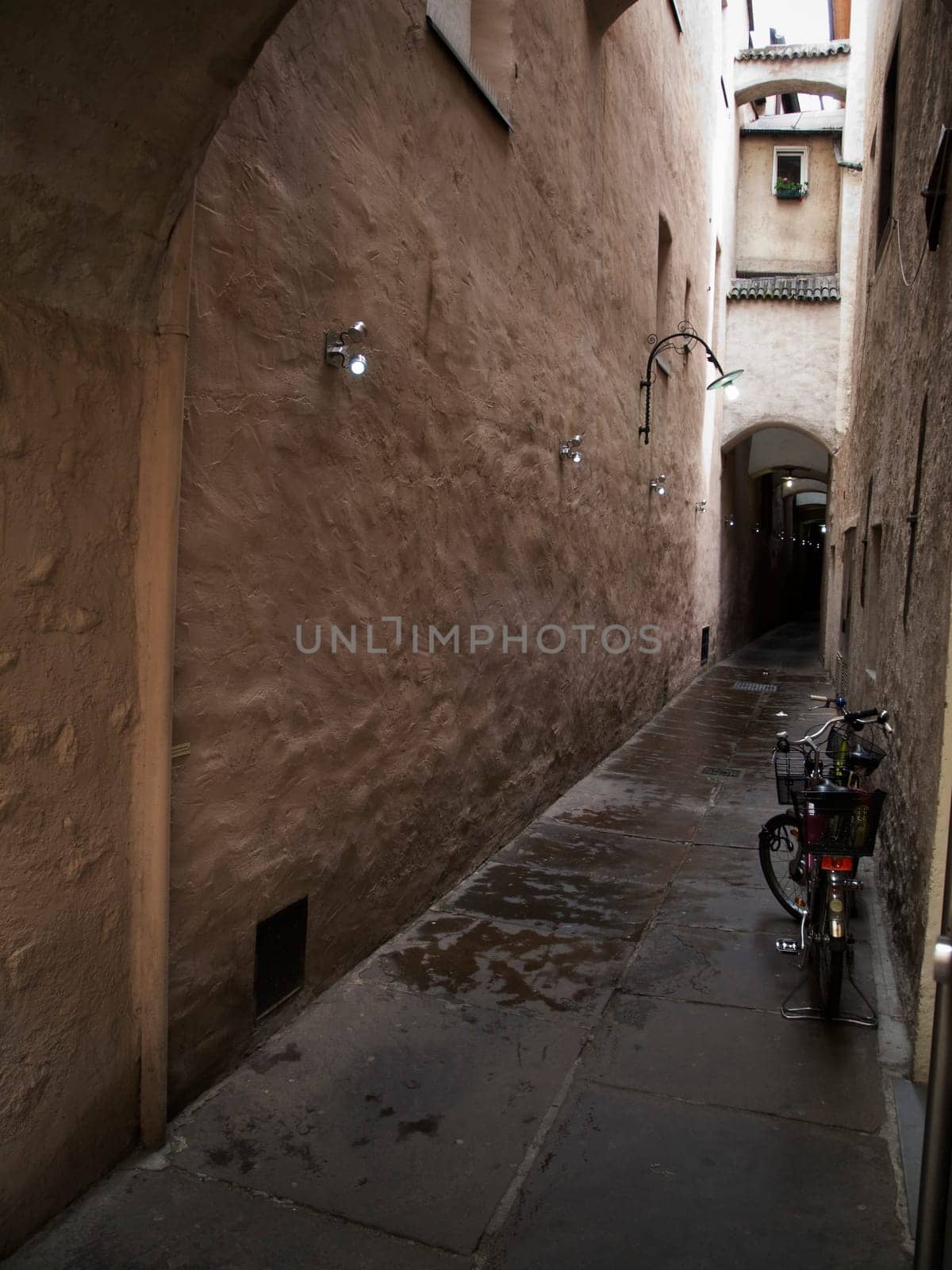View of a narrow alley with a bike leaning against the wall and small lights on the left wall in Merano / South Tyrol