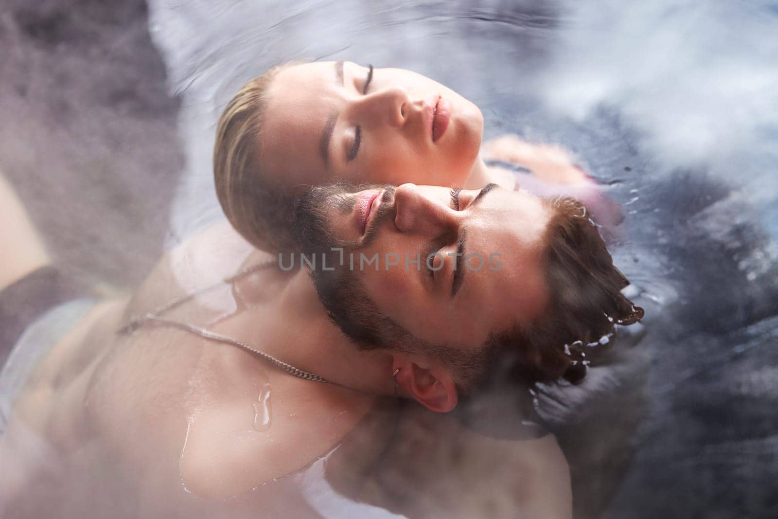 a young couple sits in a vat filled with water with their backs to each other