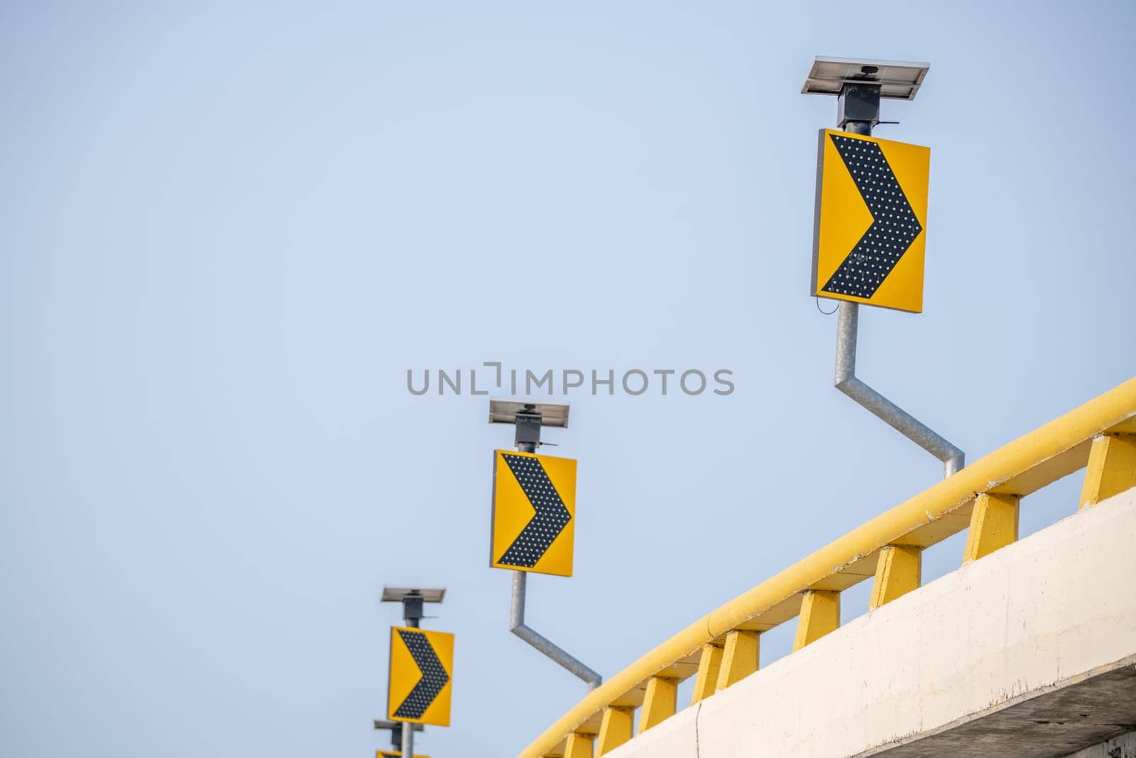 Yellow traffic signs guide drivers along curve roads. Symbols ensure safety as they navigate the streets under the watchful blue sky. Arrow sign on signpost of highway against blue sky. by Fahroni