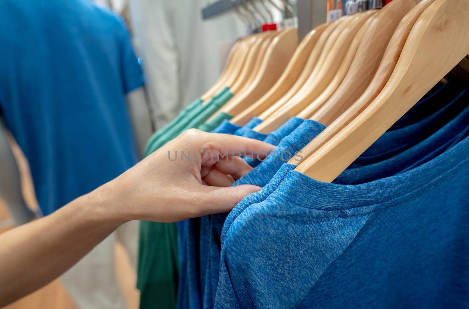 Woman shopping shirt in clothing store. Woman choosing clothes. Shirt on hanger hanging on rack in clothing store. Fashion retail shop inside shopping mall. Clothes on hangers in a clothes shop. by Fahroni