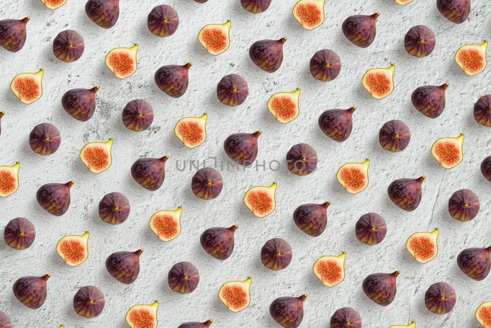 Top view of rows of whole and halves figs on stone table