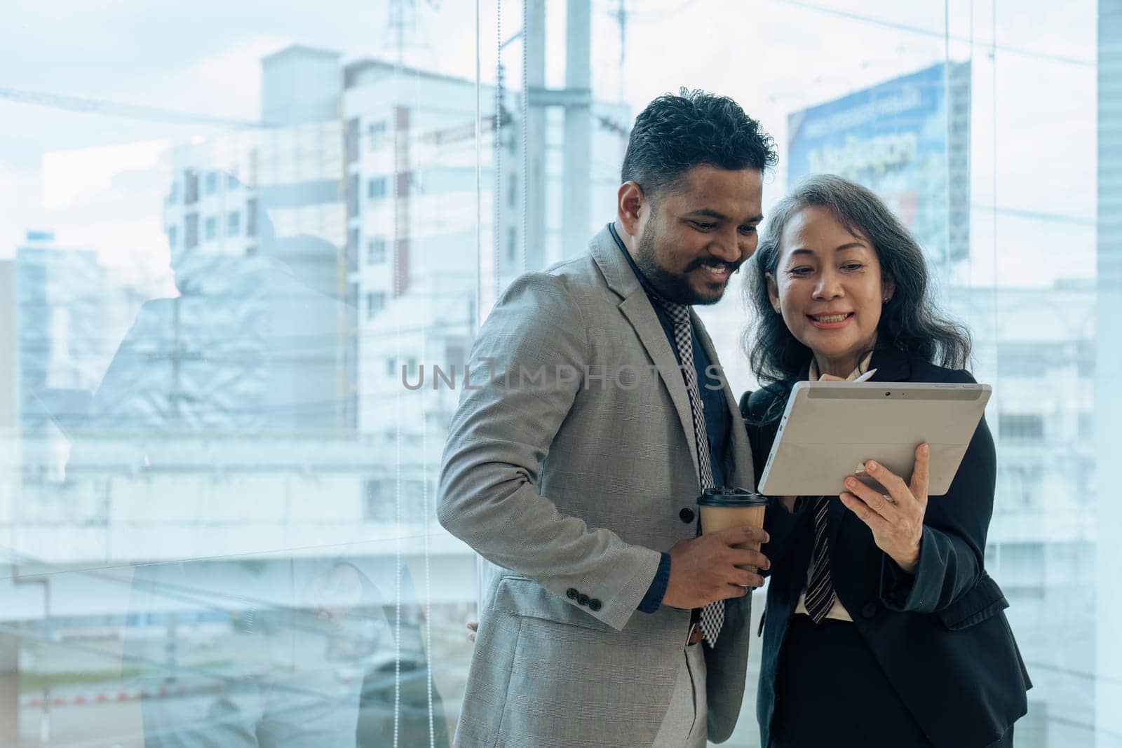 Two happy diverse coworker discussing report on tablet, working on project together.