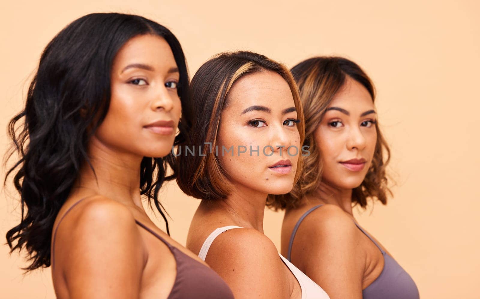 Diversity, beauty and portrait of women in row with self love, solidarity and pride in studio together. Face, group of people on beige background with underwear, skincare and cosmetics for hair care. by YuriArcurs