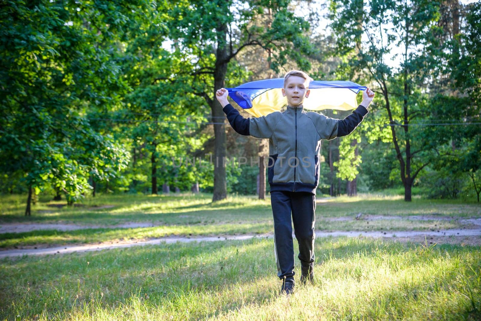 Pray for Ukraine. boy with Ukrainian flag running the summer park. Little kid waving national flag praying for peace. Happy child celebrating Independence Day.