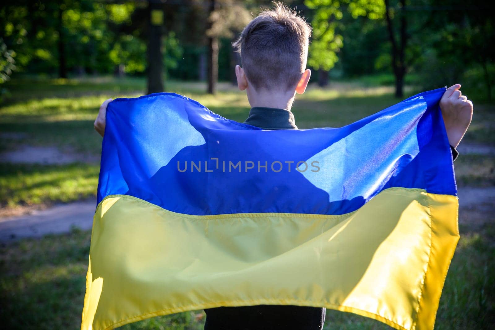 Pray for Ukraine. boy with Ukrainian flag running the summer park. Little kid waving national flag praying for peace. Happy child celebrating Independence Day.