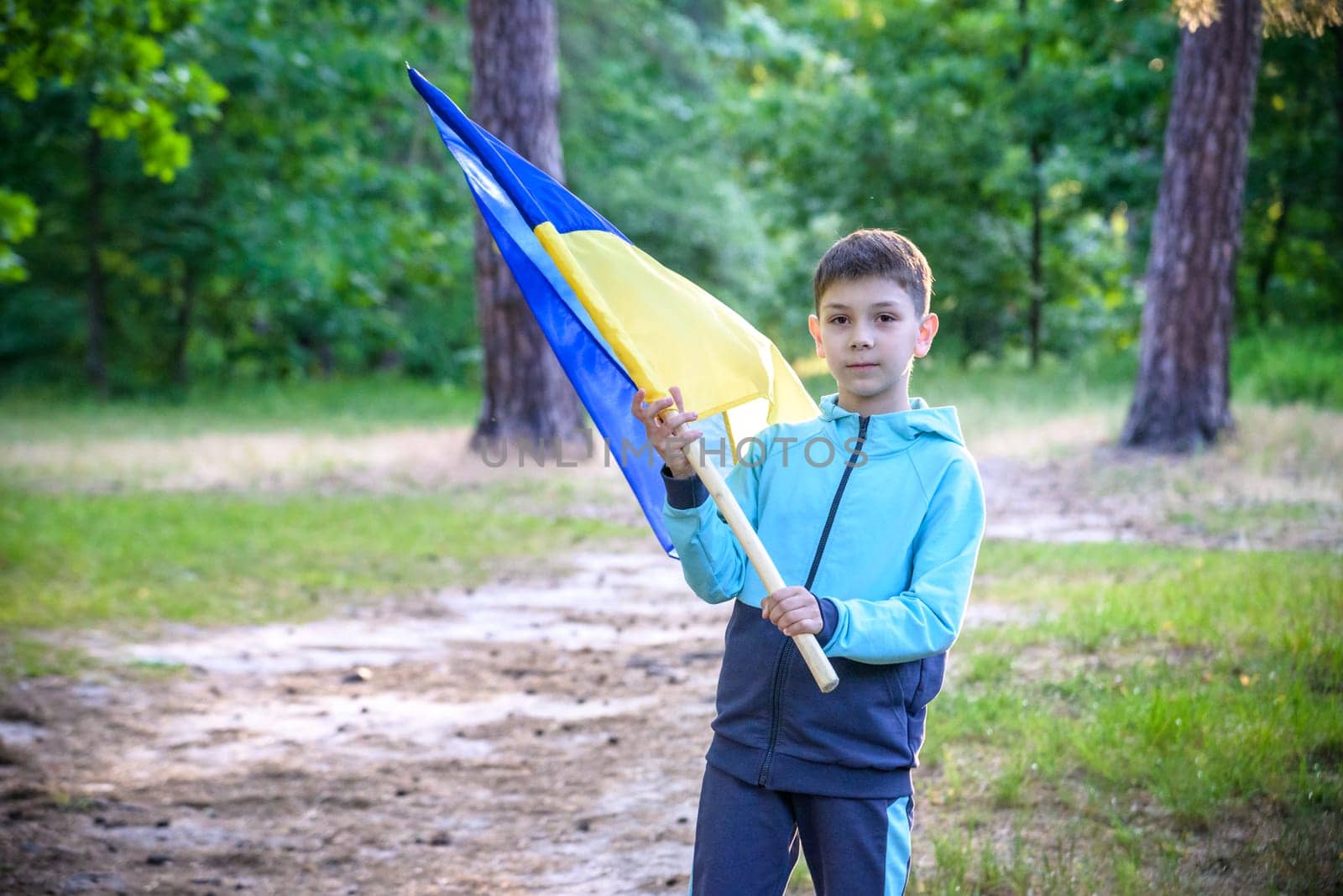 Ukrainian boy with waving flag and praying to stop the war in Ukraine in a field at sunset. War of Russia against Ukraine. Stop War.