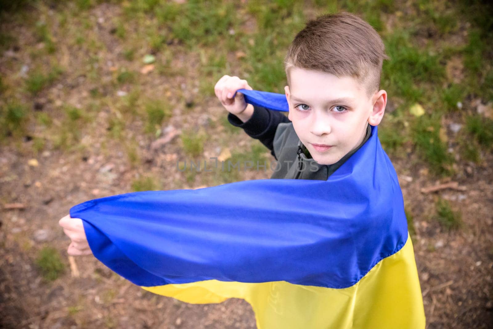 Ukrainian boy with waving flag and praying to stop the war in Ukraine in a field at sunset. War of Russia against Ukraine. Stop War.