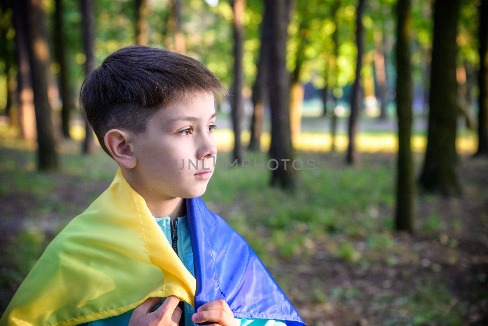 Worried teenager patriot wear blue yellow Ukrainian flag on his shoulders. Spring nature background. Ukraine national symbol. Patriotism.