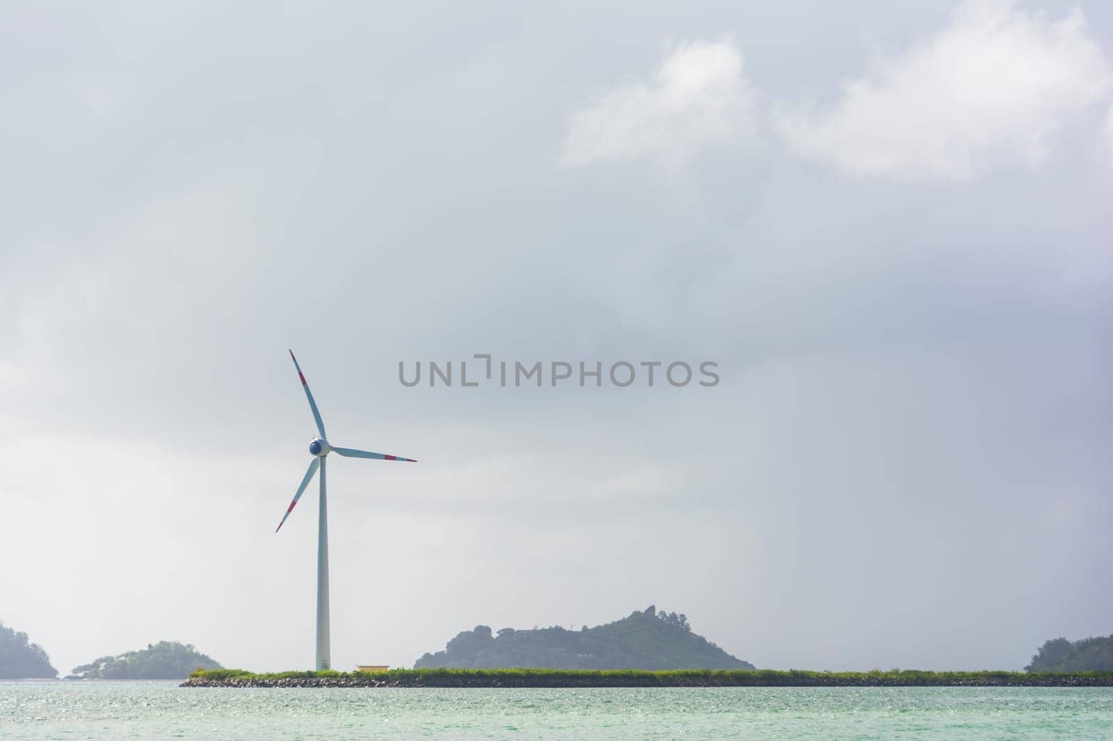 Wind turbine on an offshore coastal strip by the sea in front of a cloudy sky.