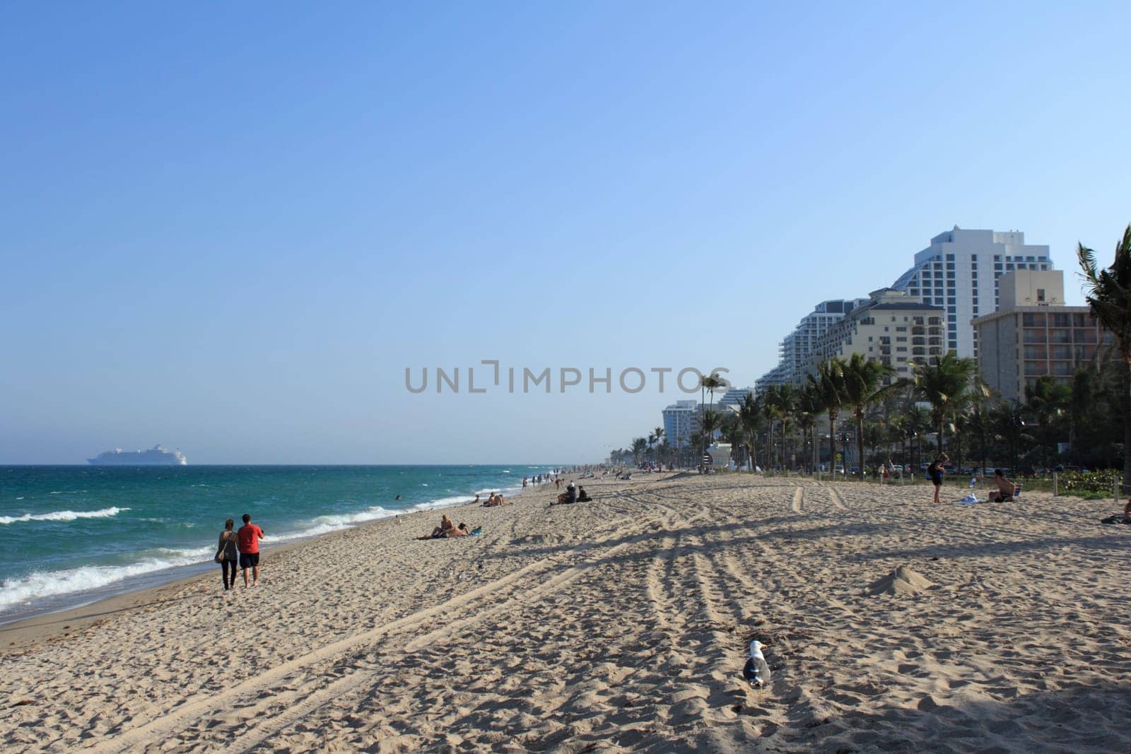 FORT LAUDERDALE, FLORIDA - MARCH 23, 2013: People enjoying an evening walk along the shores of Fort Lauderdale beach right before sunset. A cruise ship is seen on the Atlantic Ocean in background.
