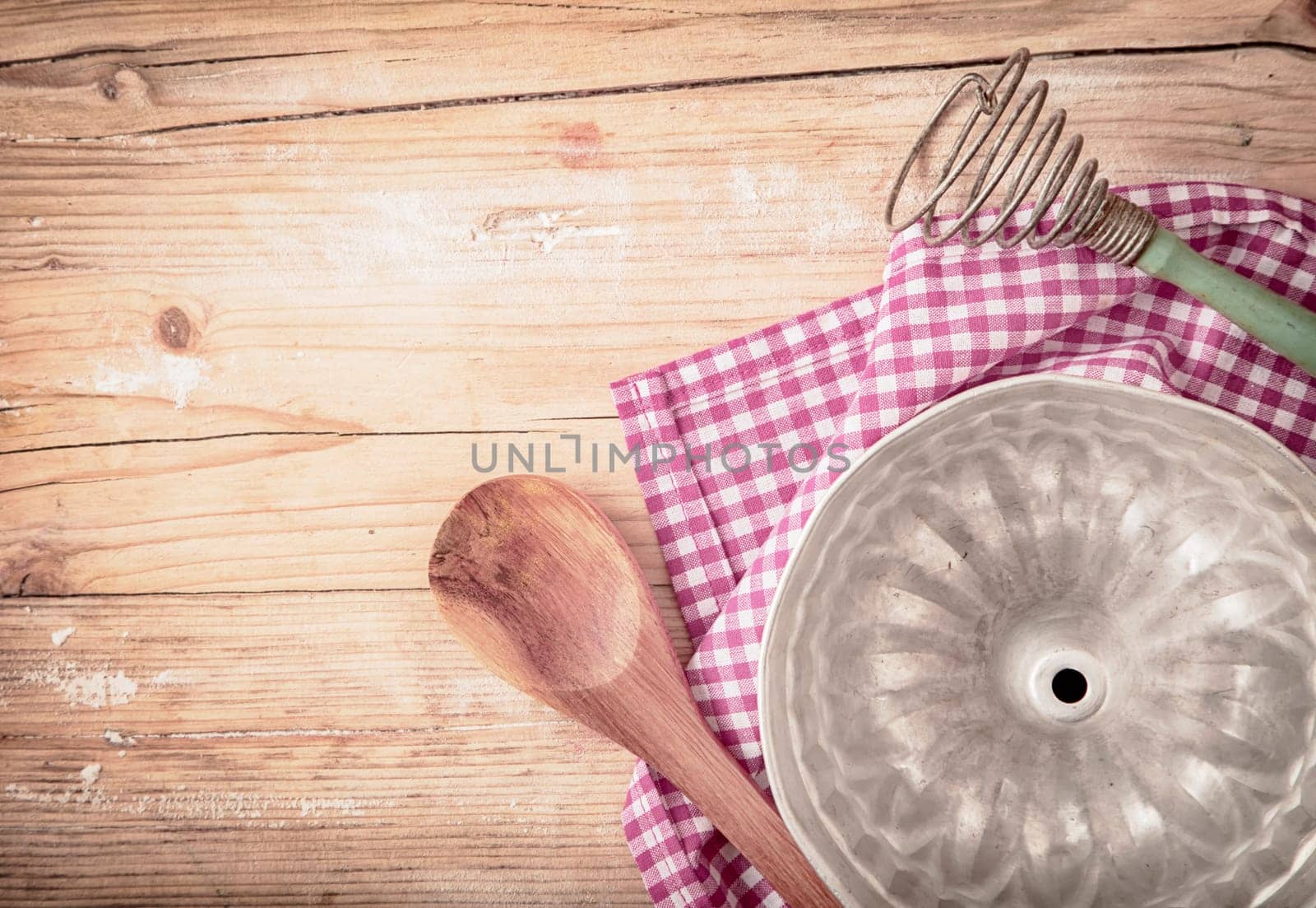 Old circular metal baking mould for cooking a ring cake or flan lying upside down on a fresh red and white checked cloth on a rustic wooden table, overhead view