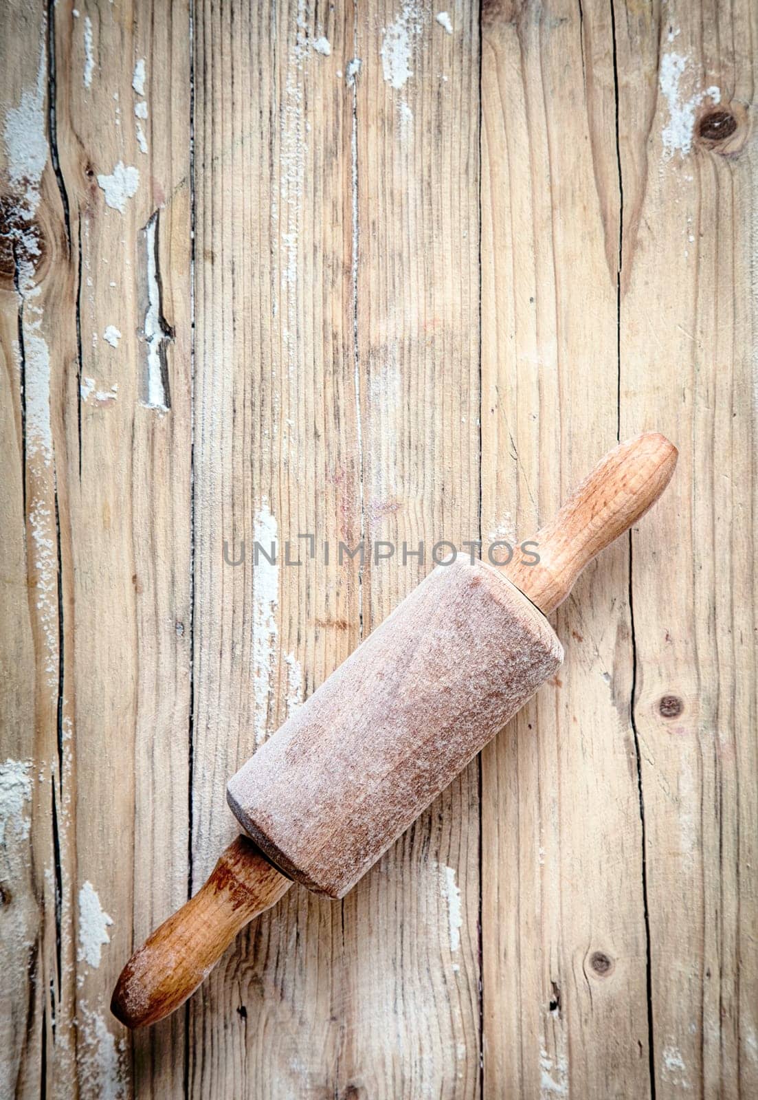 Old small wooden rolling pin covered in a thin layer of flour from baking and rolling dough lying on a wooden table in a country kitchen, overhead, view with copyspace