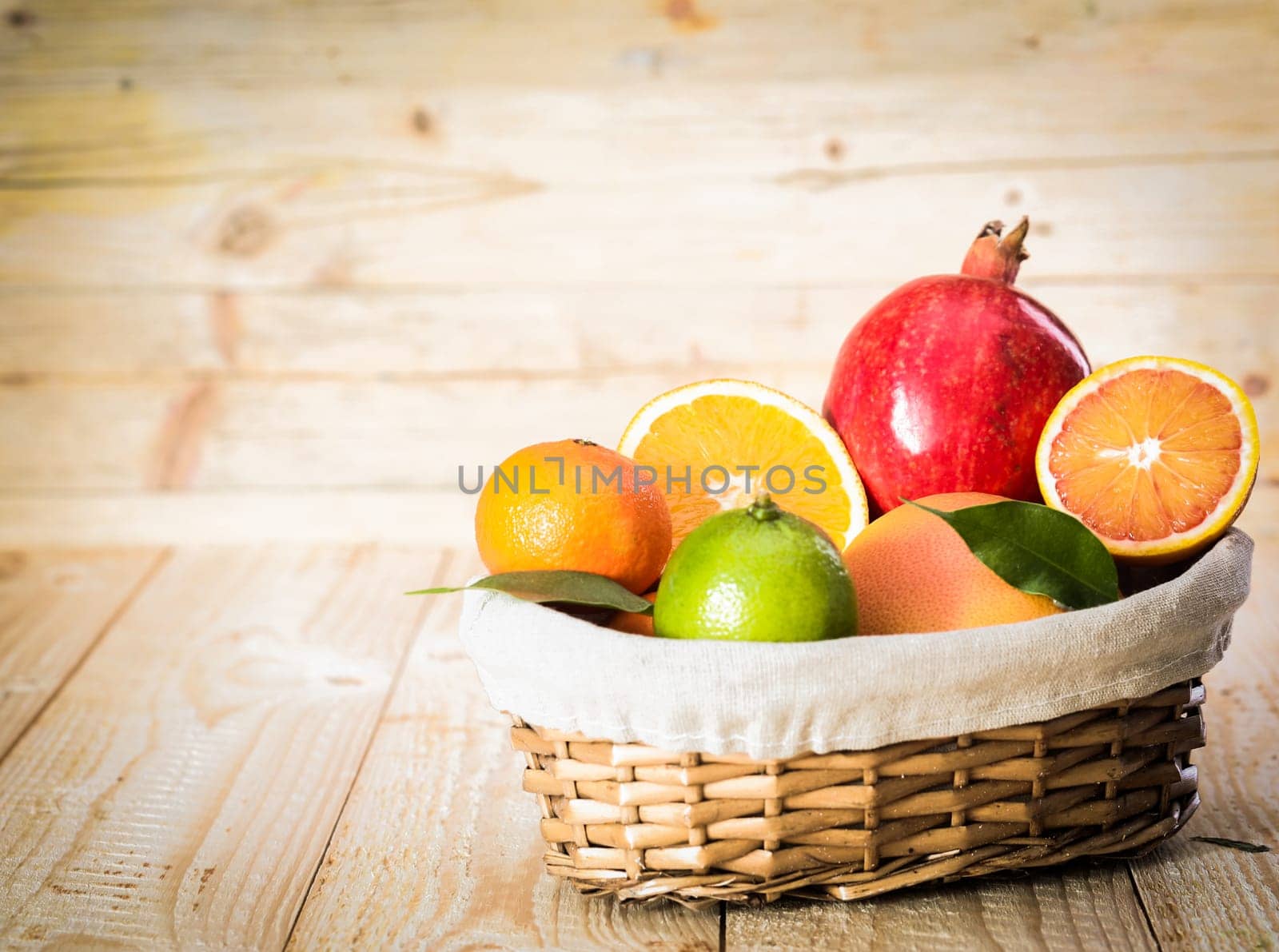 Small wicker basket of delicious assorted fresh fruit with an apple and a variety of citrus including a juicy halved orange on a wooden background