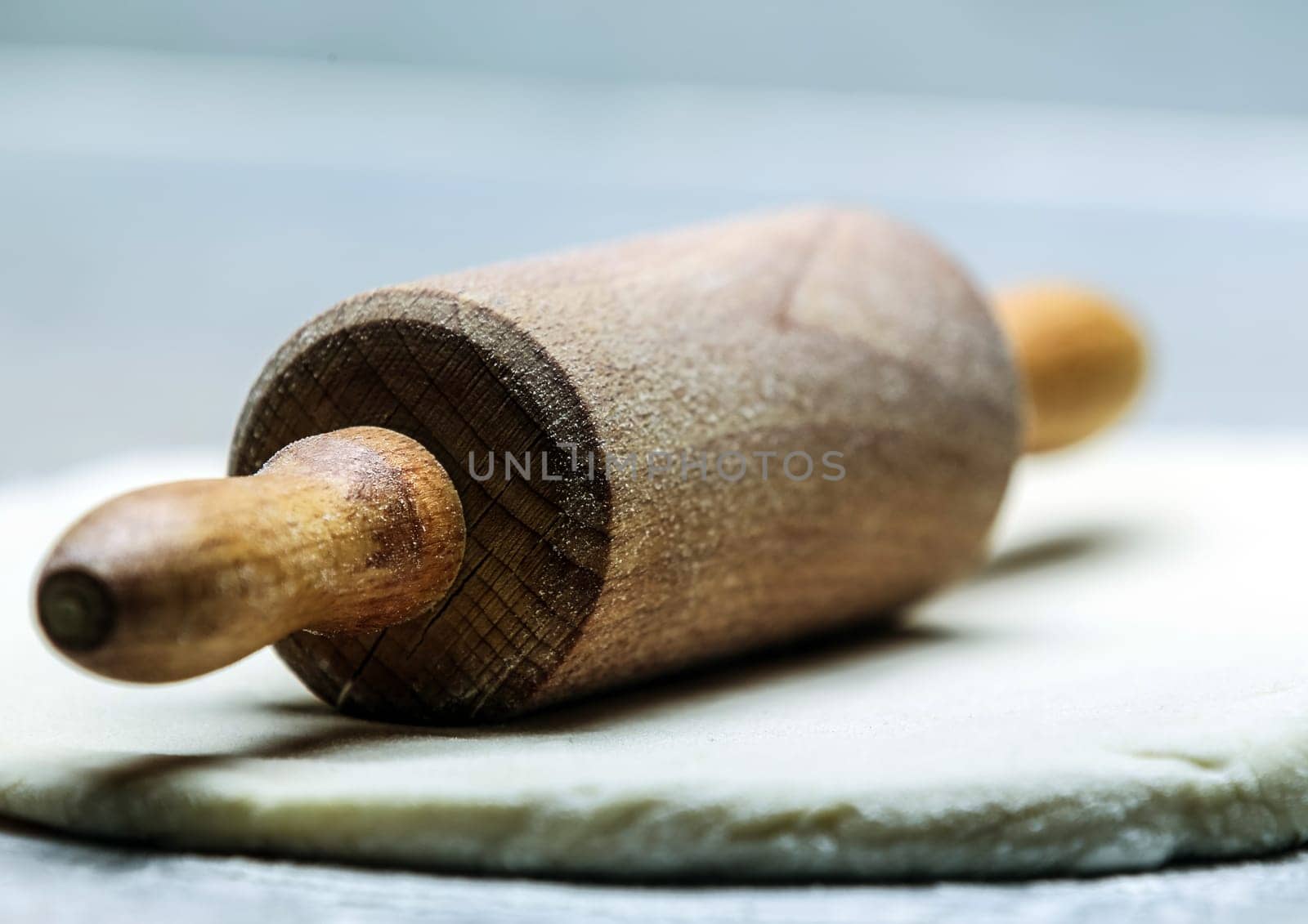 Close-up low angle view of an old-fashioned wooden rolling pin on rolled out dough or pastry resting at an oblique angle with the handle towards the camera and shallow dof
