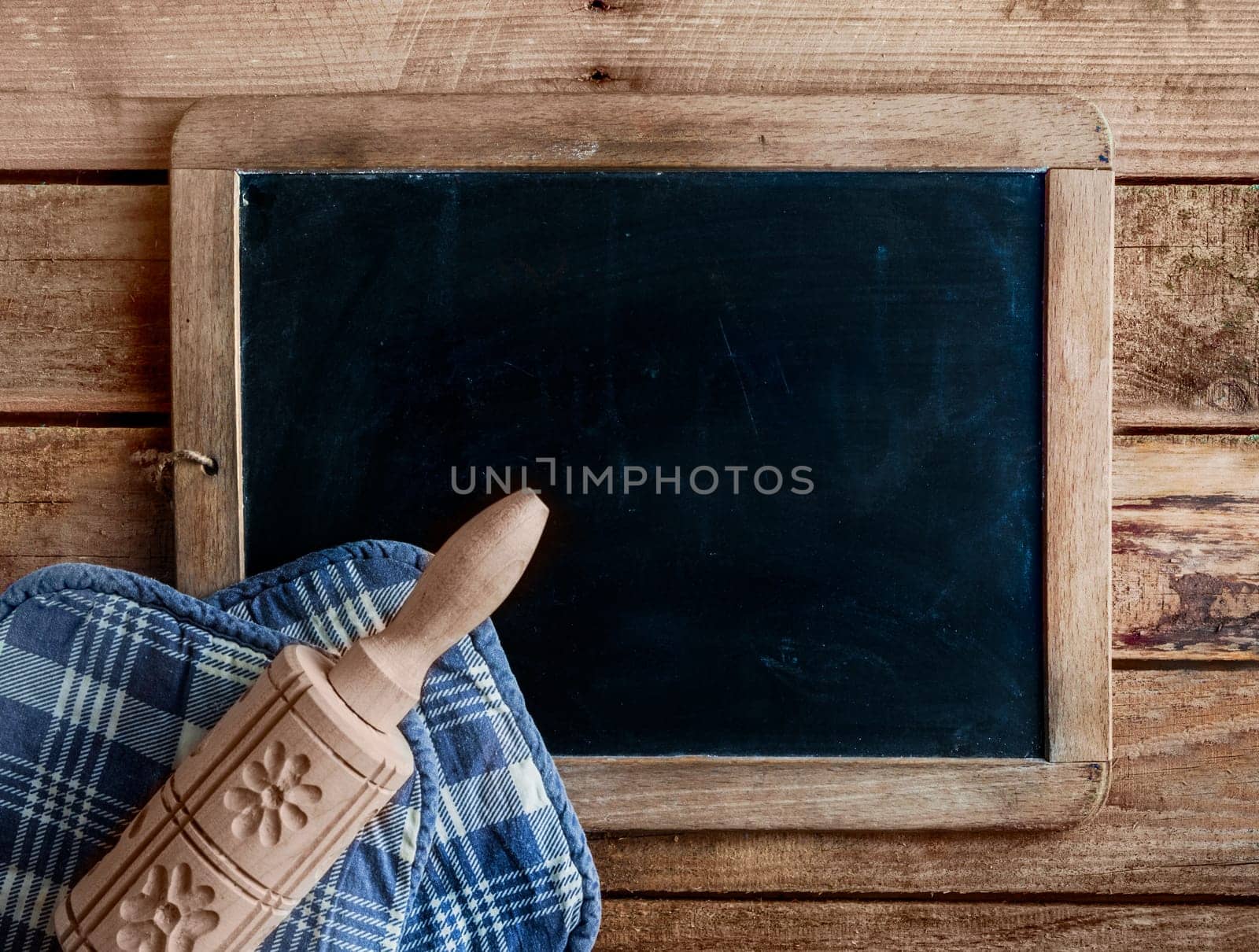 Decorative wooden rolling pin carved with patterns of flowers lying on a blue and white cloth on an blank old grunge school slate with copyspace for your menu or text