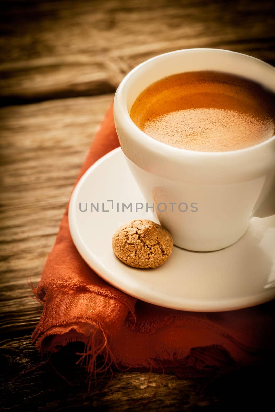 Morning coffee break with a cup of aromatic rich frothy espresso and a macaroon served in a rustic kitchen on a weathered old wooden surface, closeup high angle view