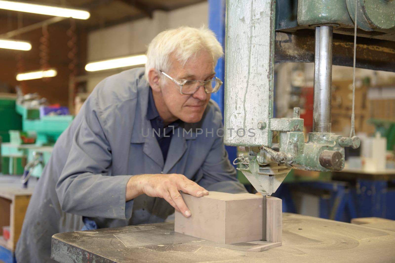 senior worker using machine cutter to saw block of wood