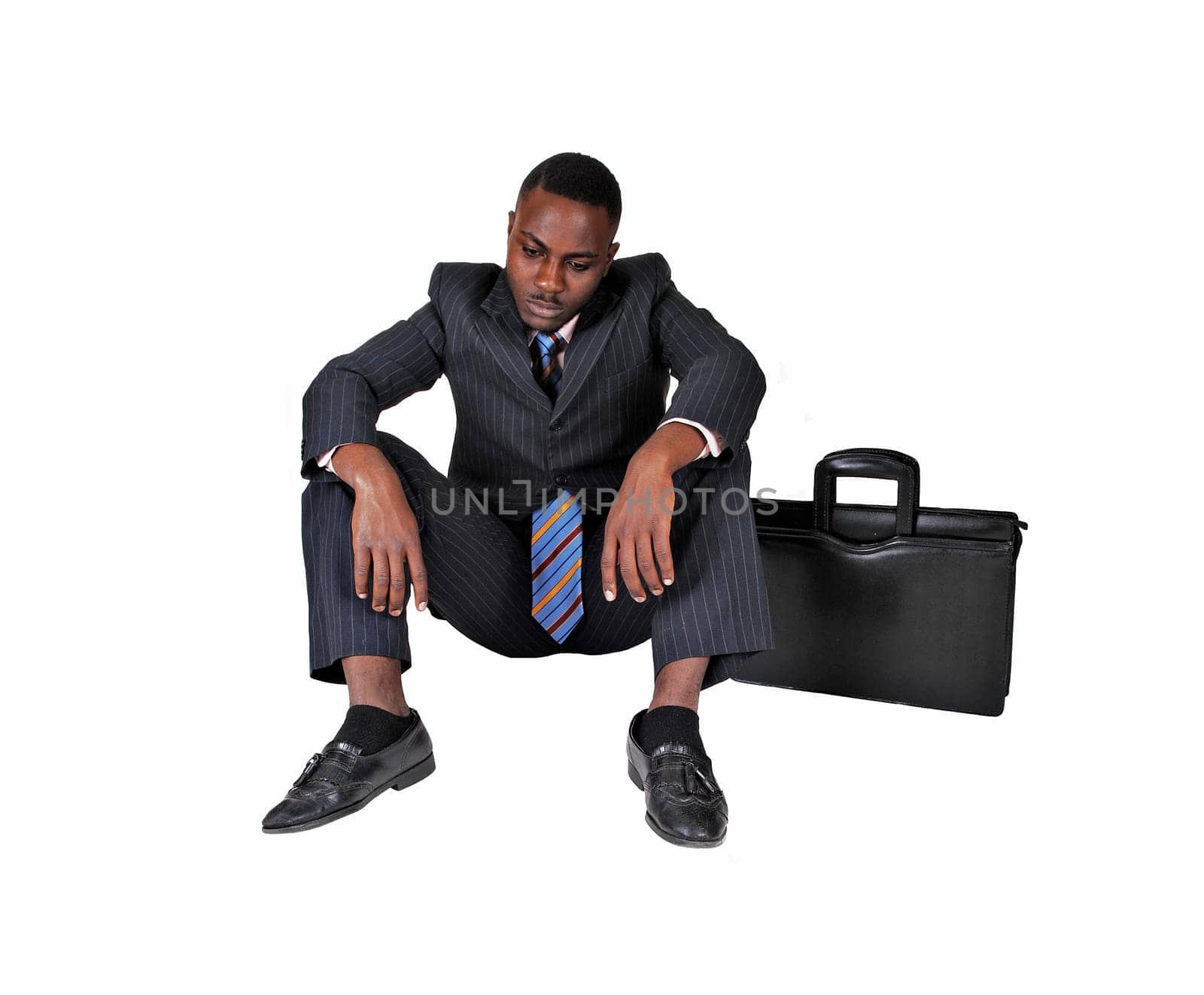 A black businessman sitting on the floor with briefcase on his side.very disappointed, over white background..