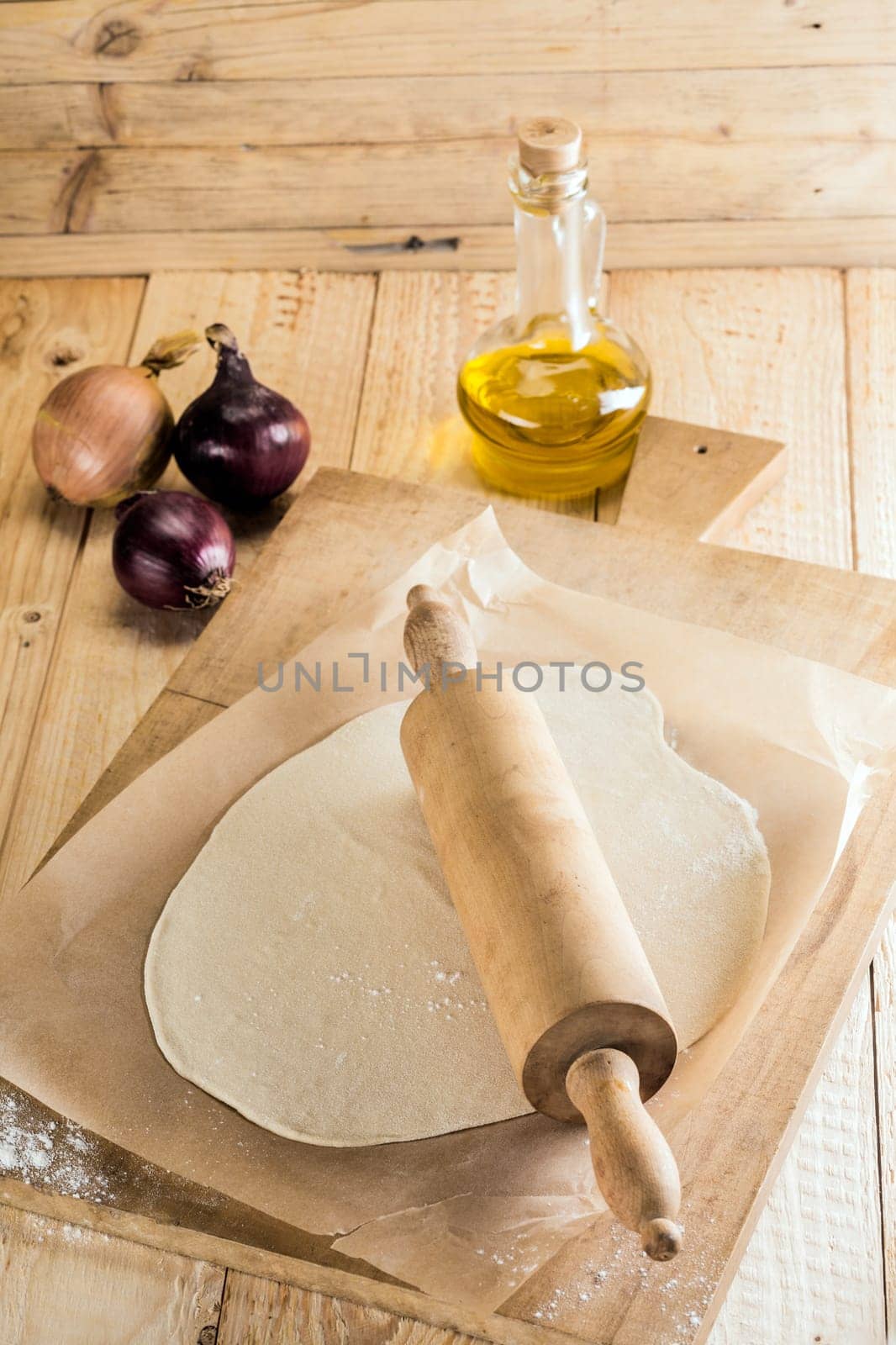 Ingredients for Italian pizza with freshly rolled dough for the pie crust or base on a wooden board with a rolling pin, onions and a decanter of olive oil