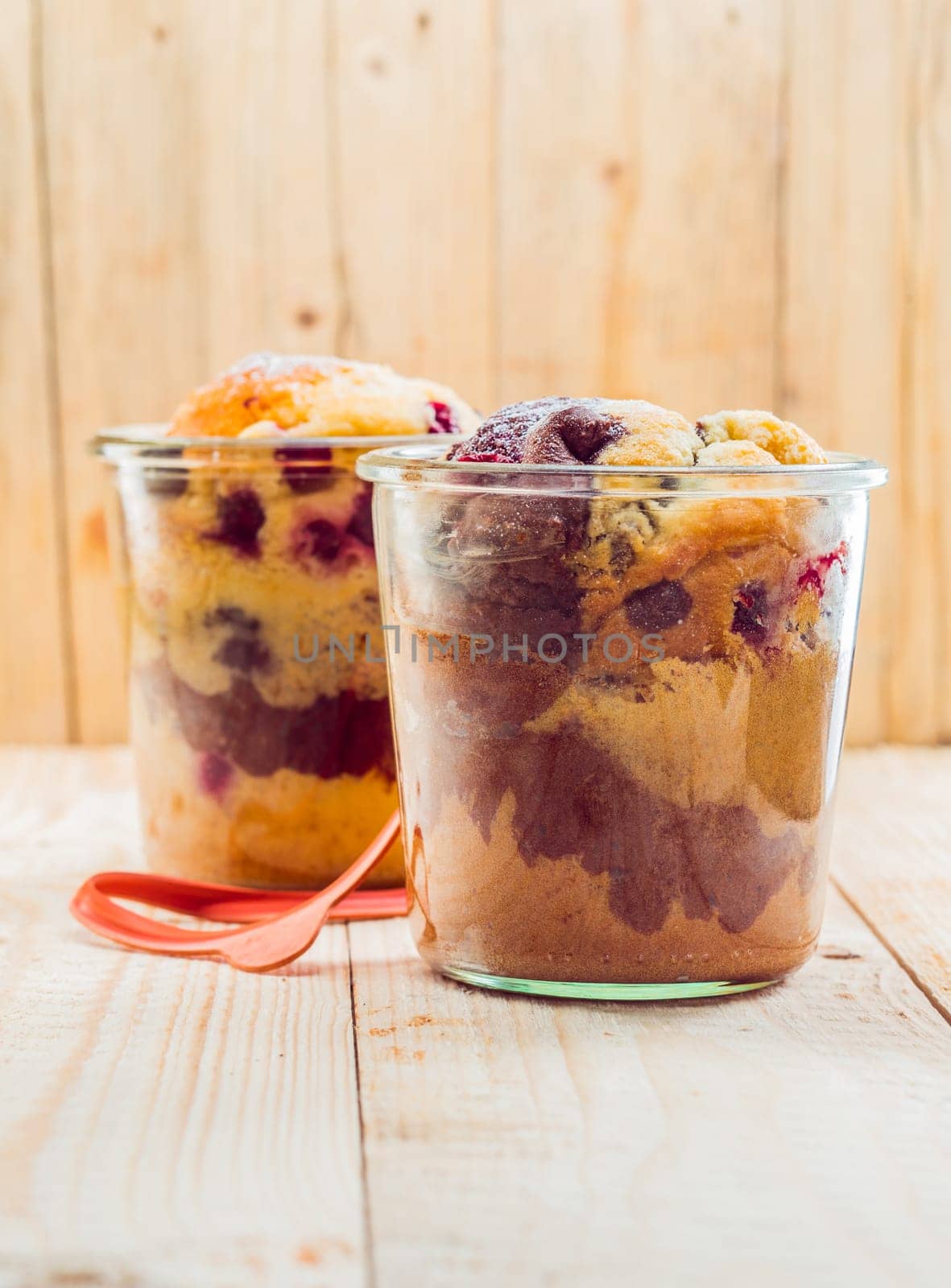 Close-up of two glasses with tasty vanilla and chocolate homemade fruitcakes, on a wooden table
